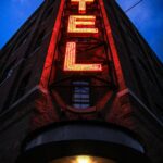 Eye-catching low angle shot of a neon hotel sign illuminating a brick building facade at dusk.