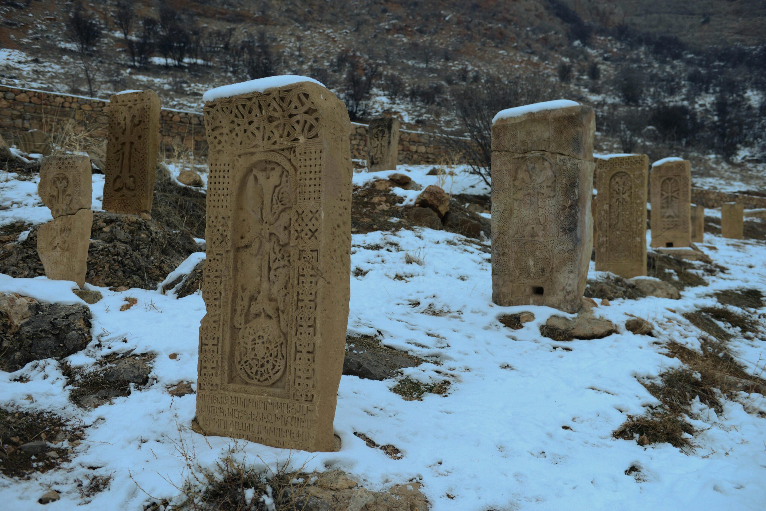 Historic Armenian tombstones covered in snow amidst rugged terrain.