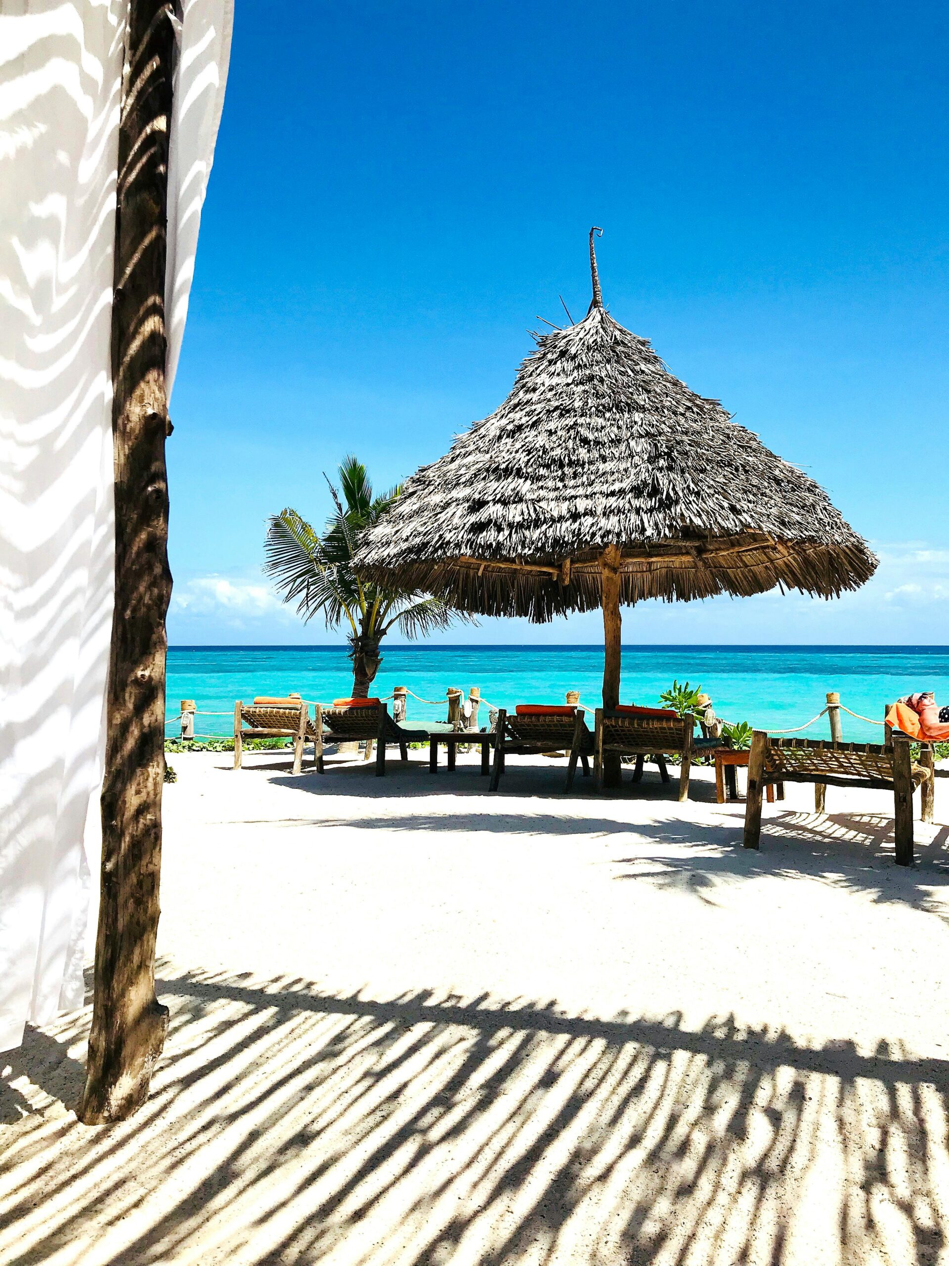 A serene tropical beach scene in Zanzibar featuring a straw umbrella and clear blue skies.