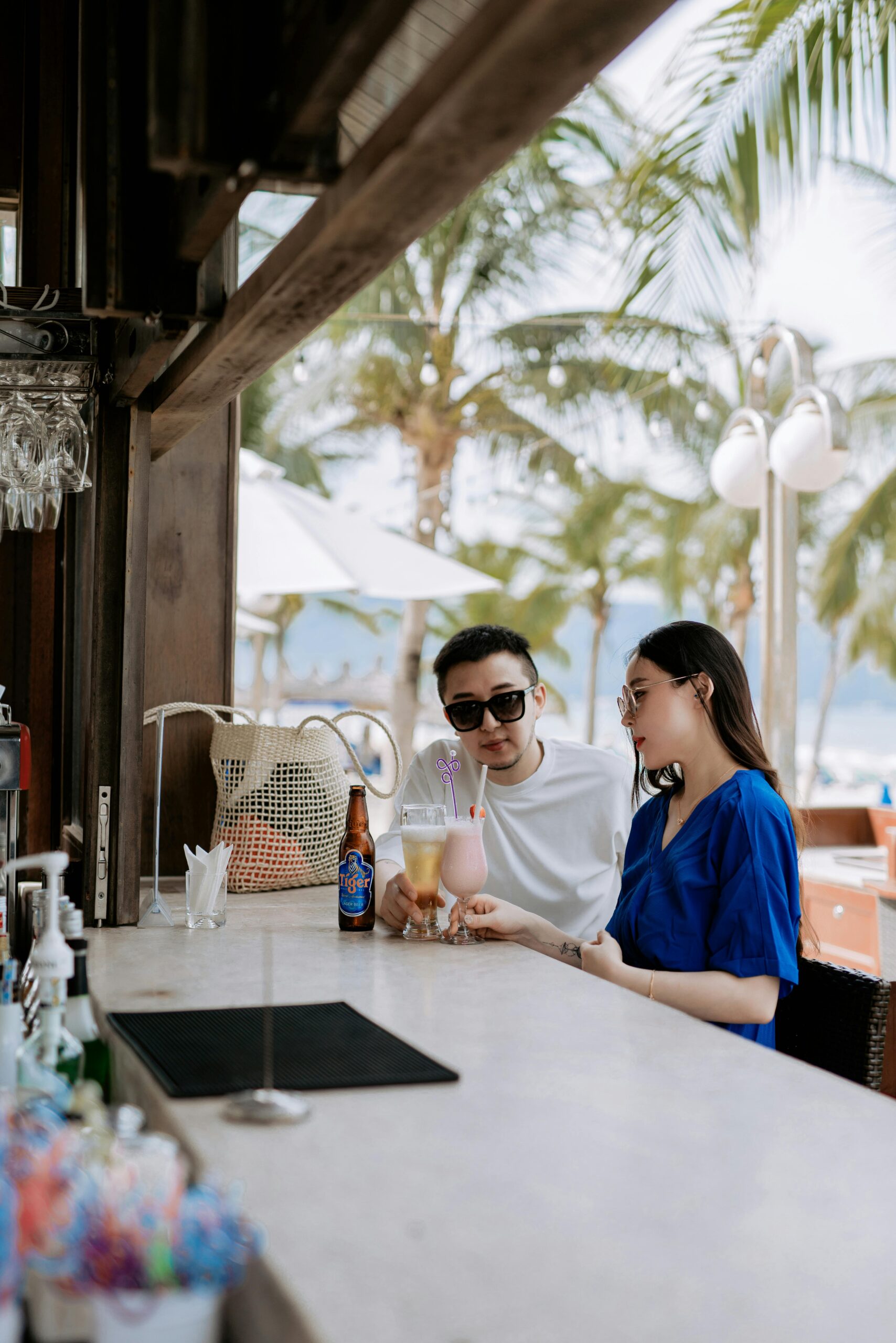 A couple relaxing with drinks at a tropical beach bar, enjoying leisure time under palm trees.