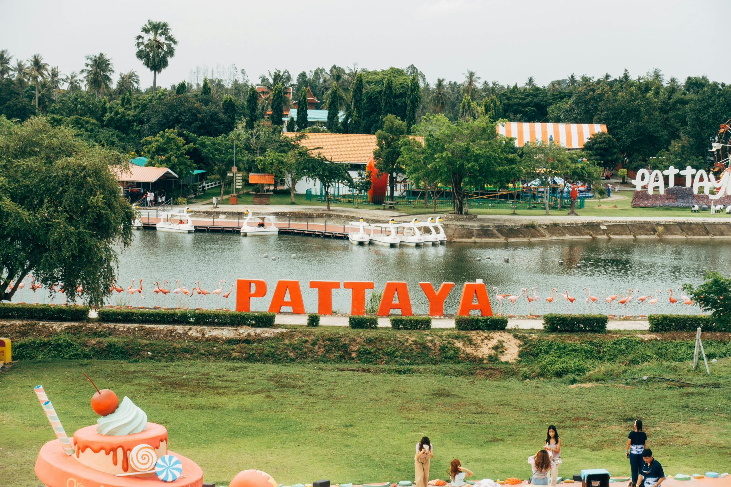A vibrant scene in Pattaya, Thailand with a lake, iconic sign, and colorful decorations.
