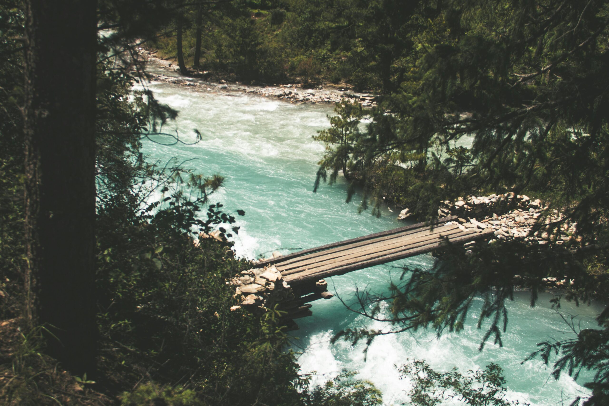 Scenic view of a wooden bridge spanning a turquoise river surrounded by lush forest in Nepal.