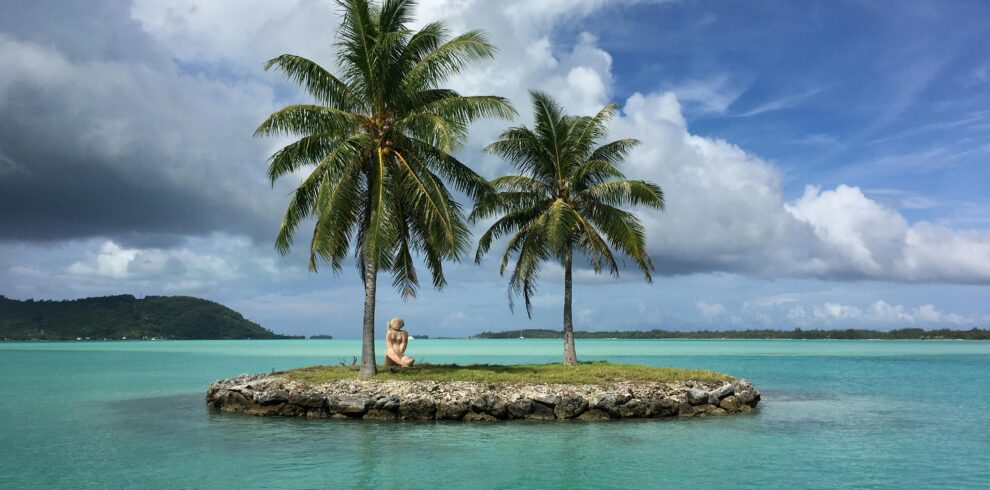 Idyllic tropical scene with a small island, palm trees, and turquoise water under a bright sky.