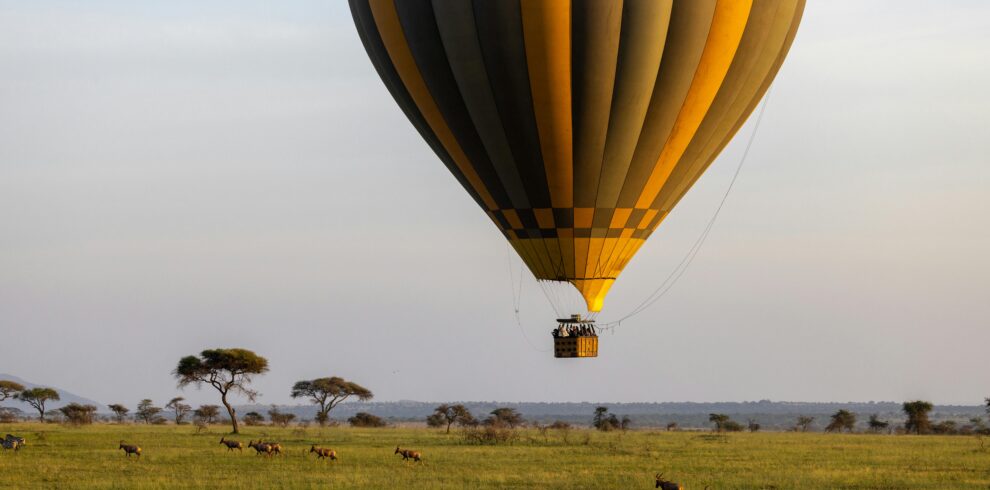 Majestic hot air balloon floats over African savannah with antelopes below.