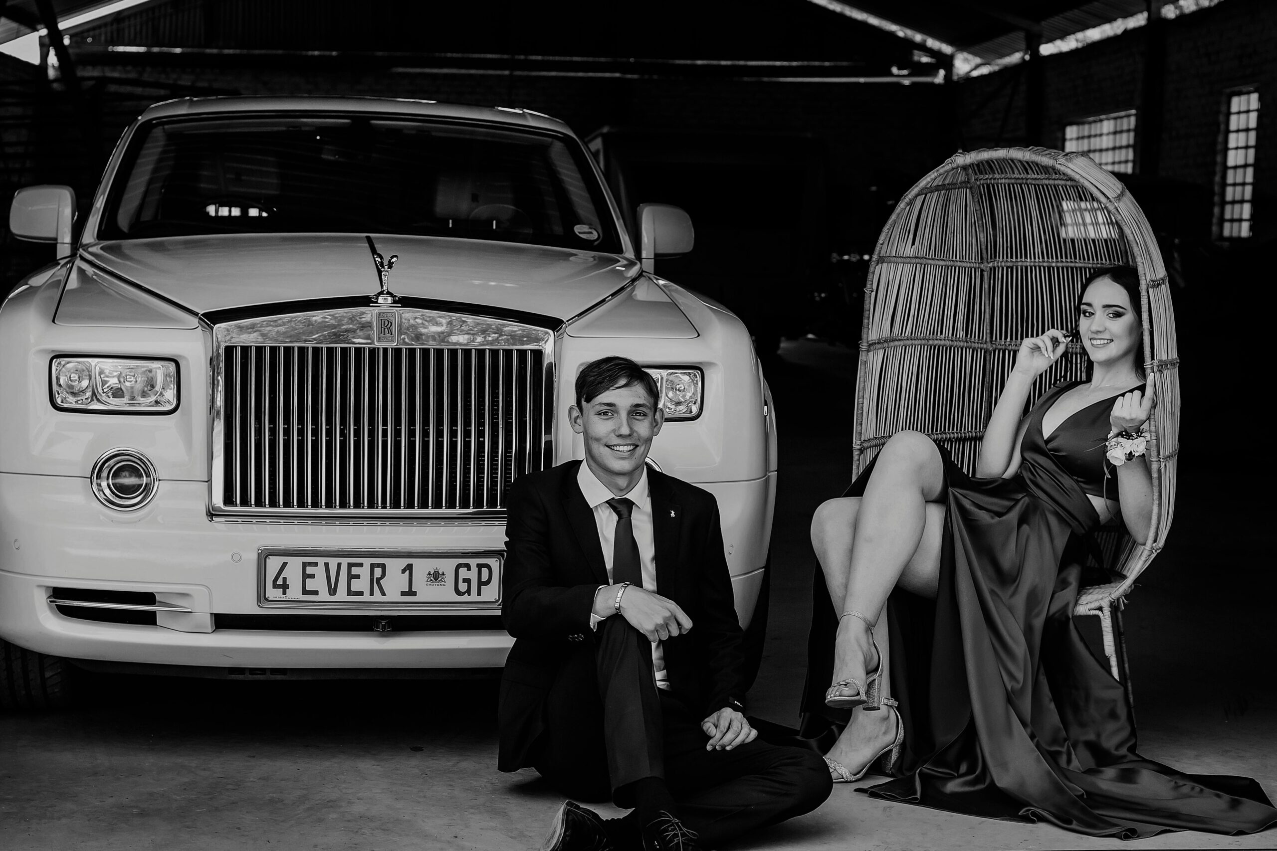 Sophisticated couple elegantly posing by a luxury car in a monochrome setting.