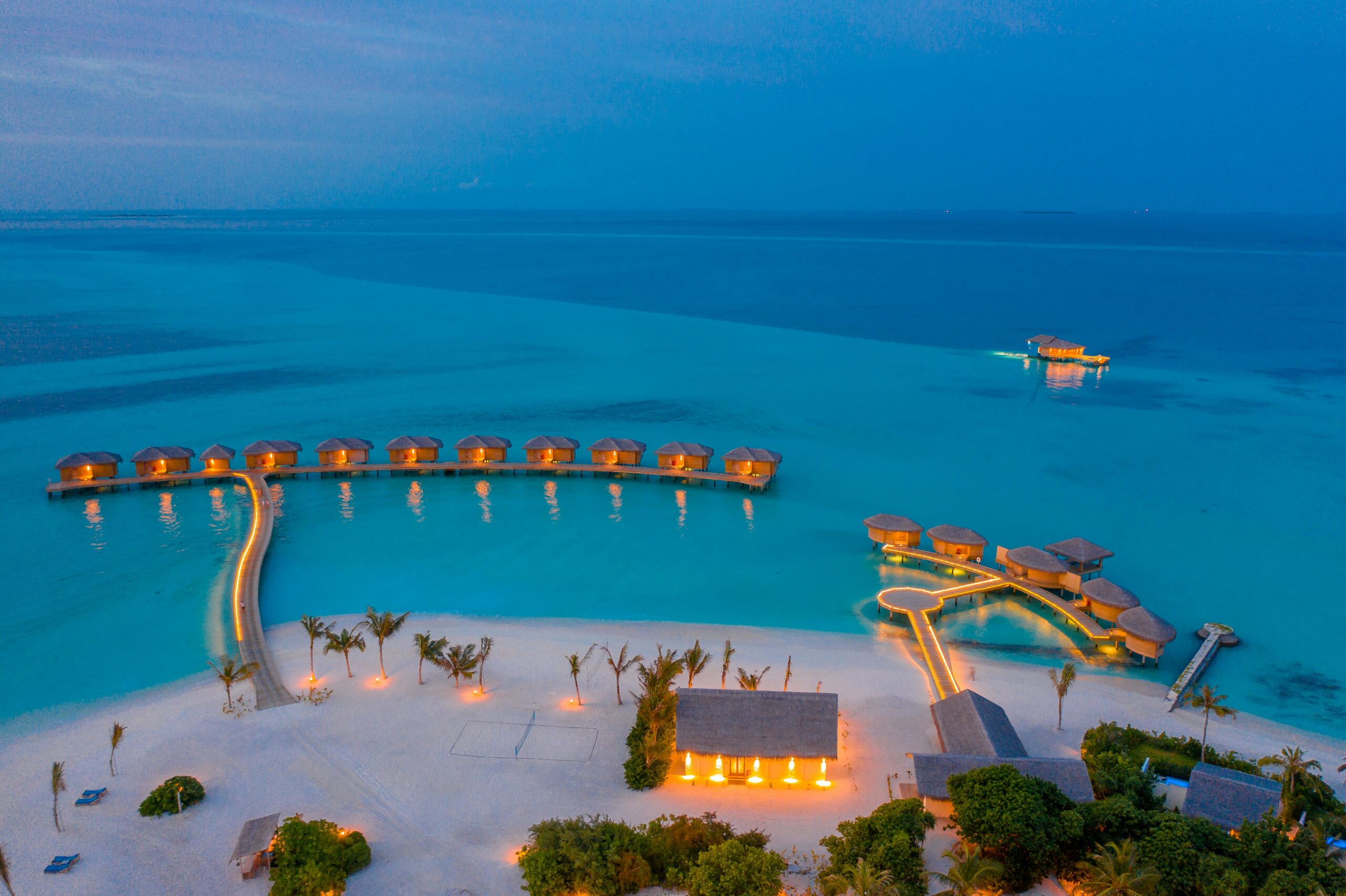 Aerial view of overwater villas illuminated at twilight in the Maldives, showcasing a serene tropical paradise.