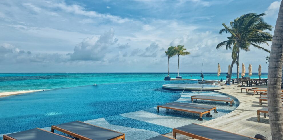 Relax by the stunning infinity pool at a luxury resort in the Maldives, surrounded by turquoise waters and palm trees.