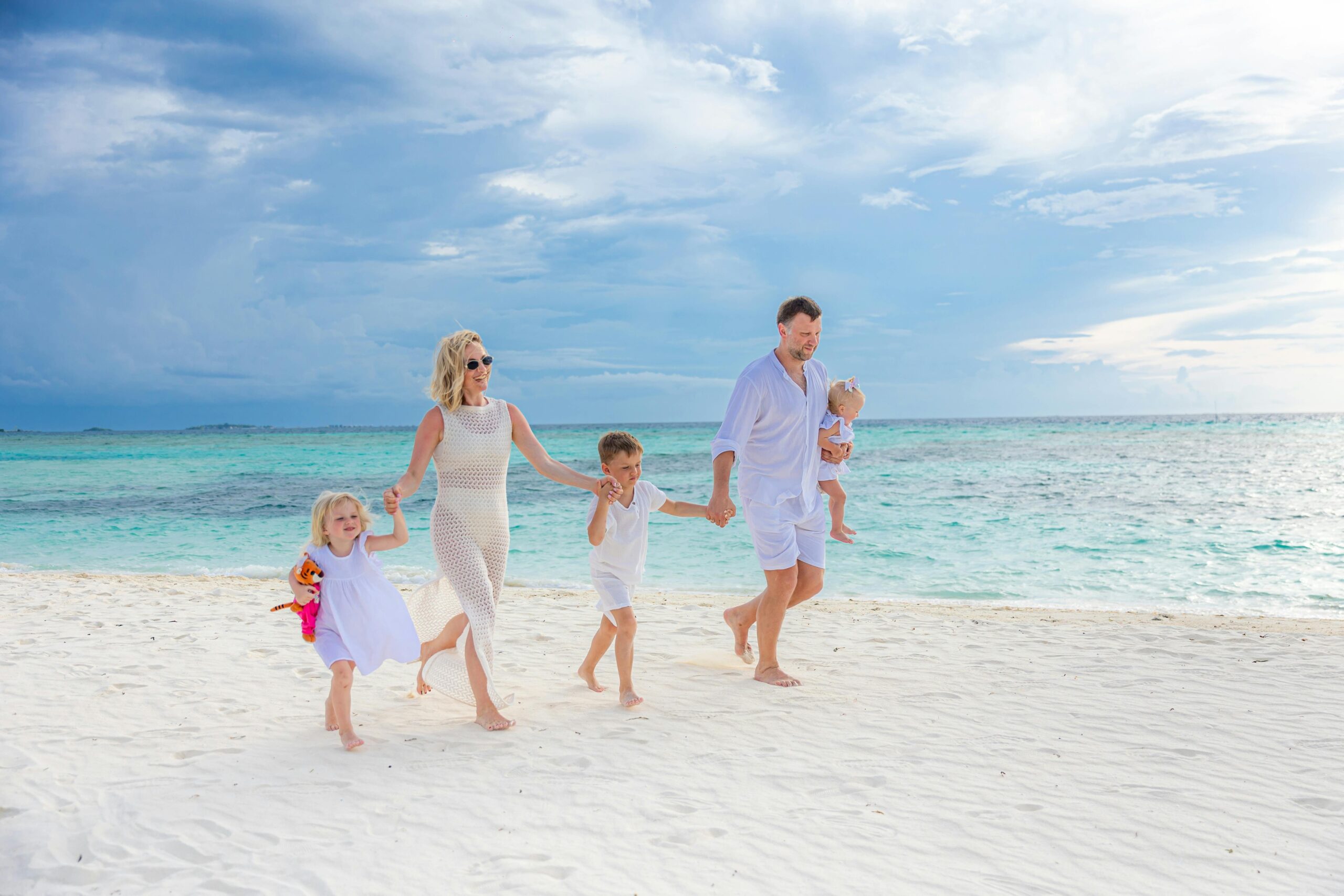 Family enjoying a walk on a pristine beach with turquoise waters, captured in a light-hearted moment.
