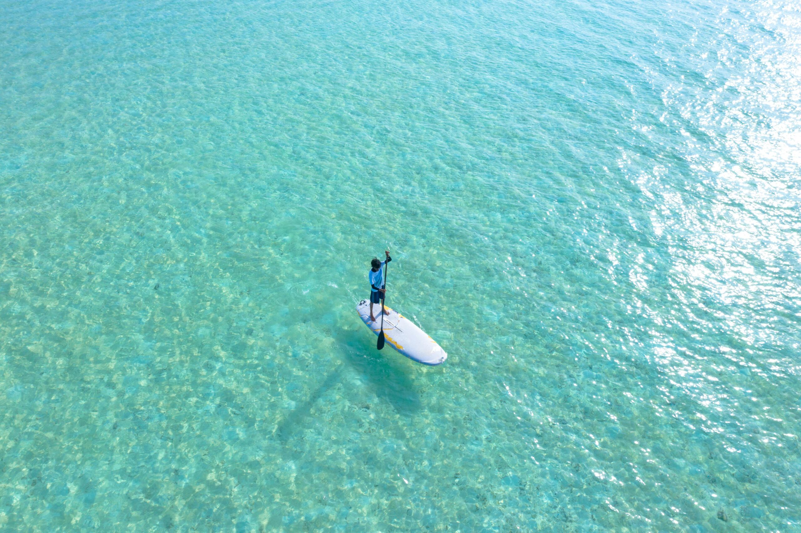 A person paddleboarding on serene, crystal-clear turquoise waters under bright daylight.
