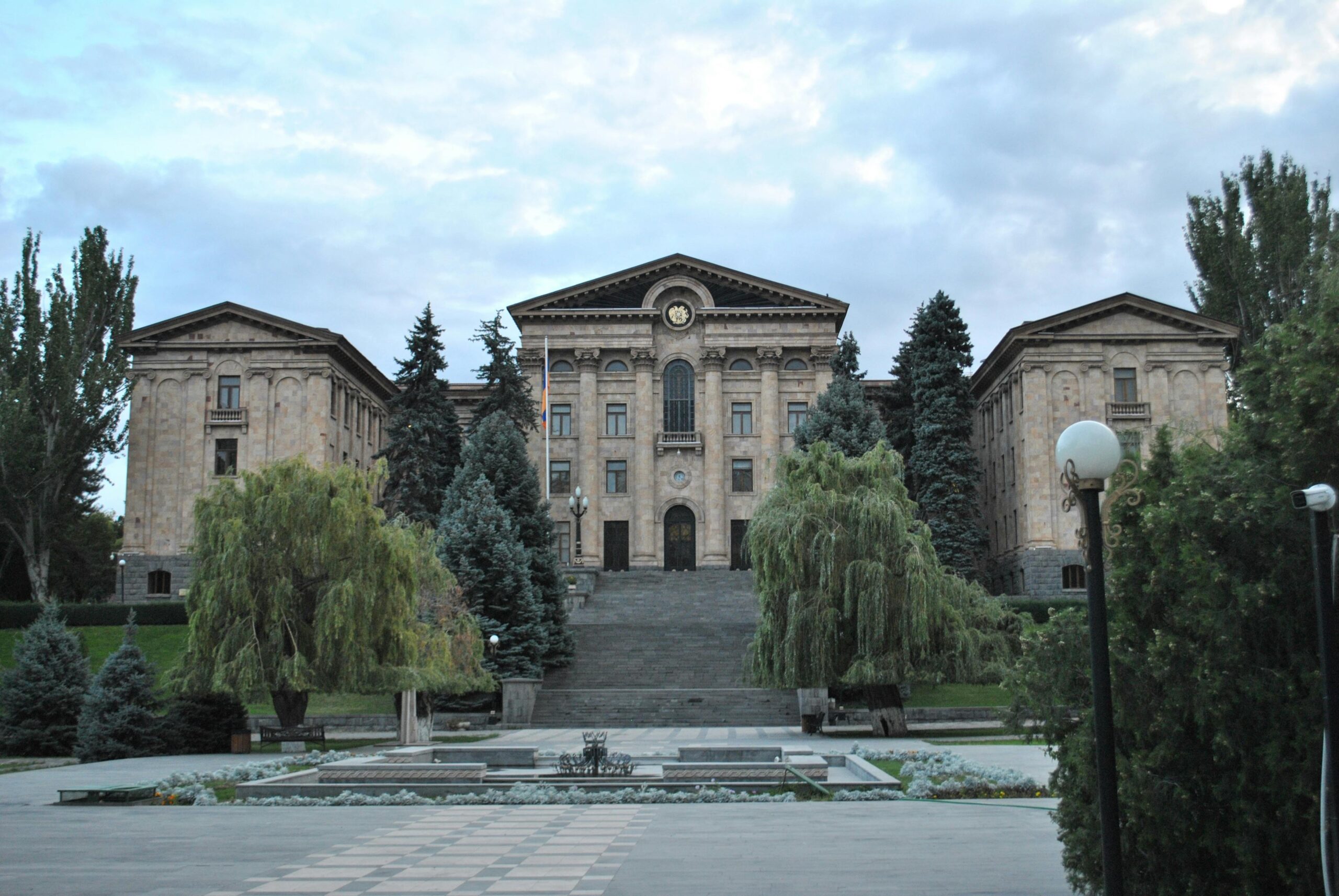 Historic government building in Yerevan, framed by greenery, under a cloudy sky.