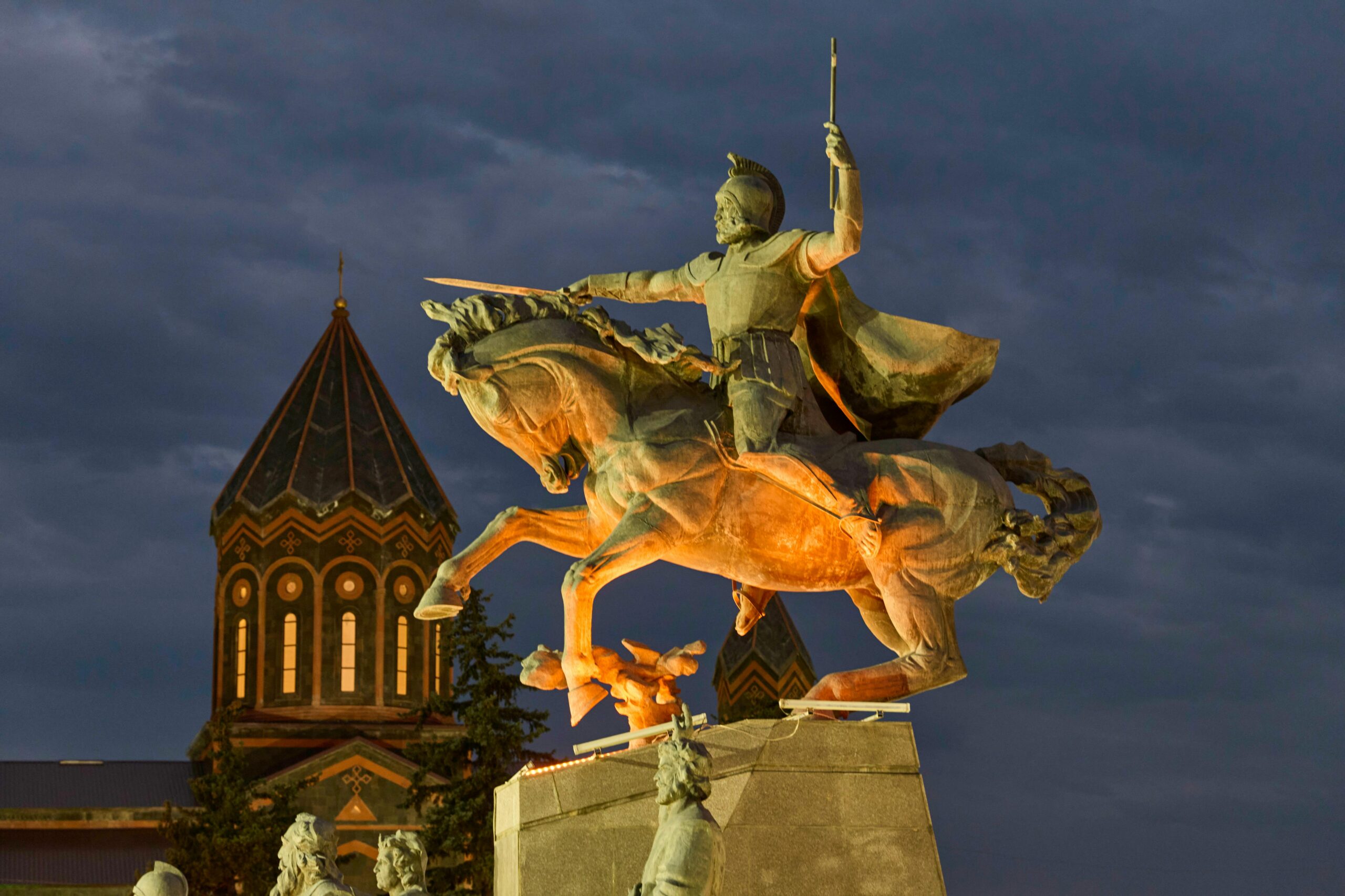 Illuminated equestrian statue in Gyumri, Armenia at dusk, displaying historical architecture.