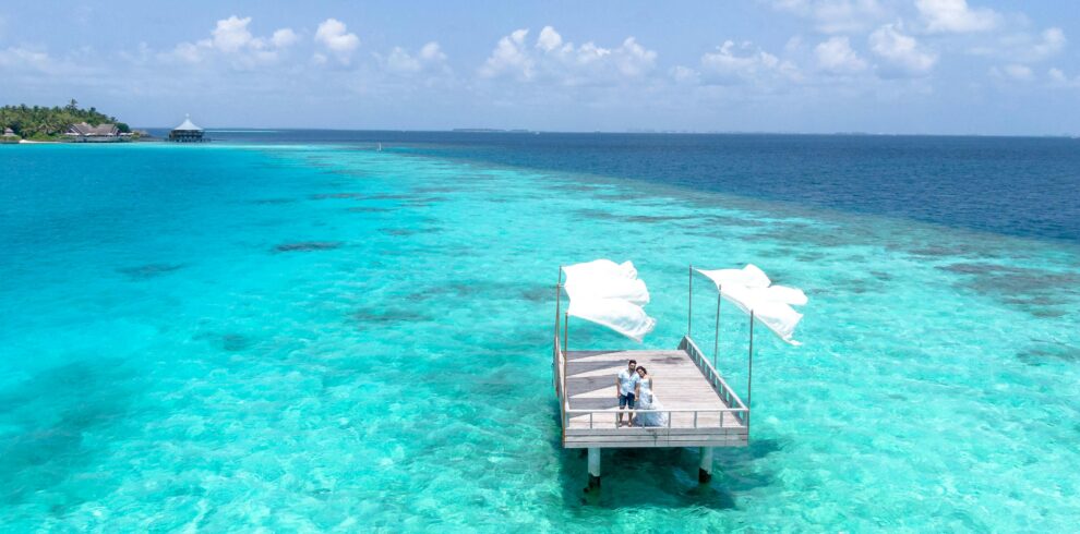 Aerial view of a couple on a deck above the turquoise waters of the Maldives, capturing a romantic moment.