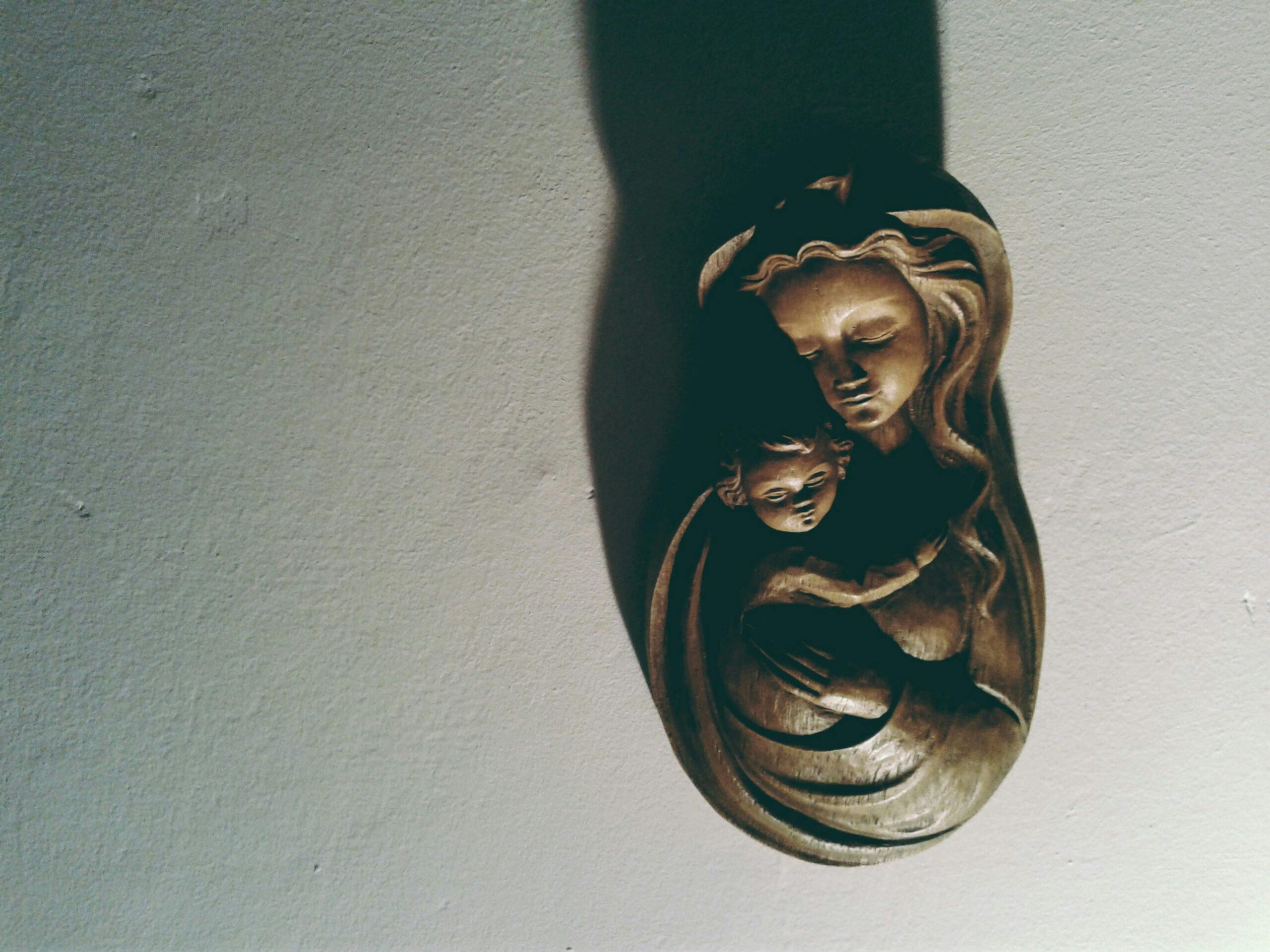Intricate wooden sculpture of mother and child casting a shadow on the wall.