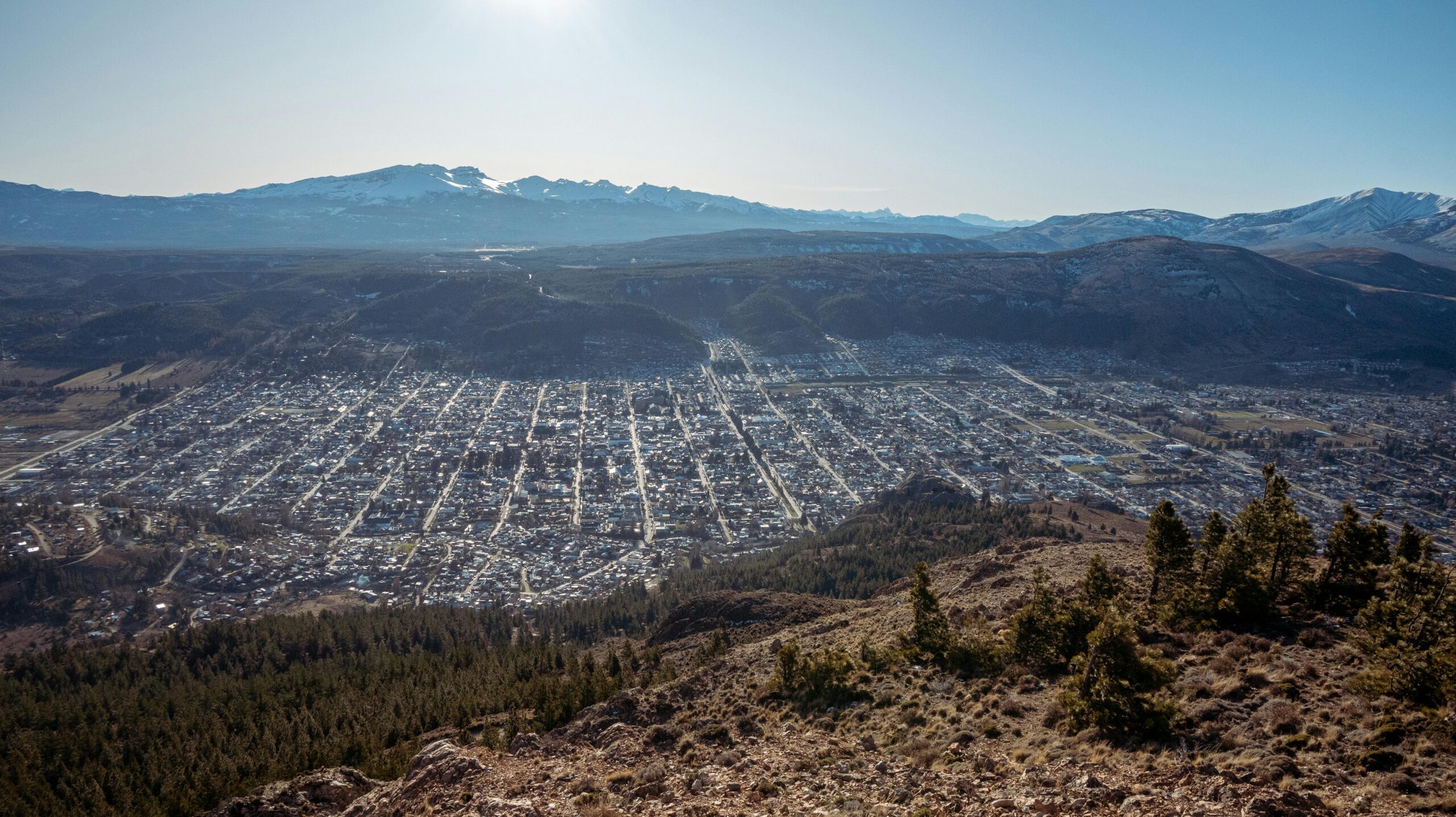 A sweeping aerial view of a city nestled in a mountainous landscape, showcasing a grid pattern with serene surroundings.