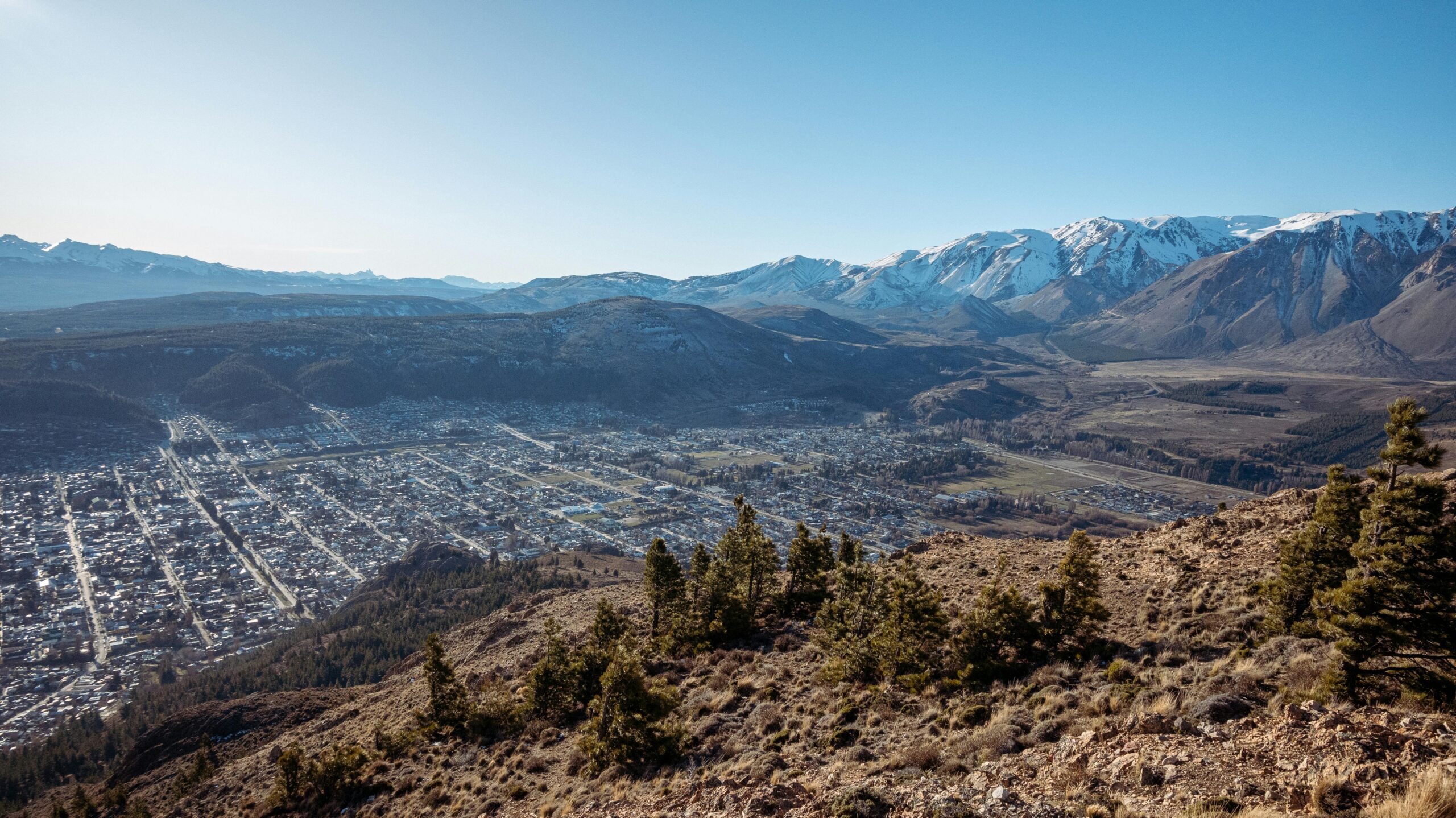A breathtaking panoramic view of Esquel, Argentina, with snow-capped mountains and clear blue skies.