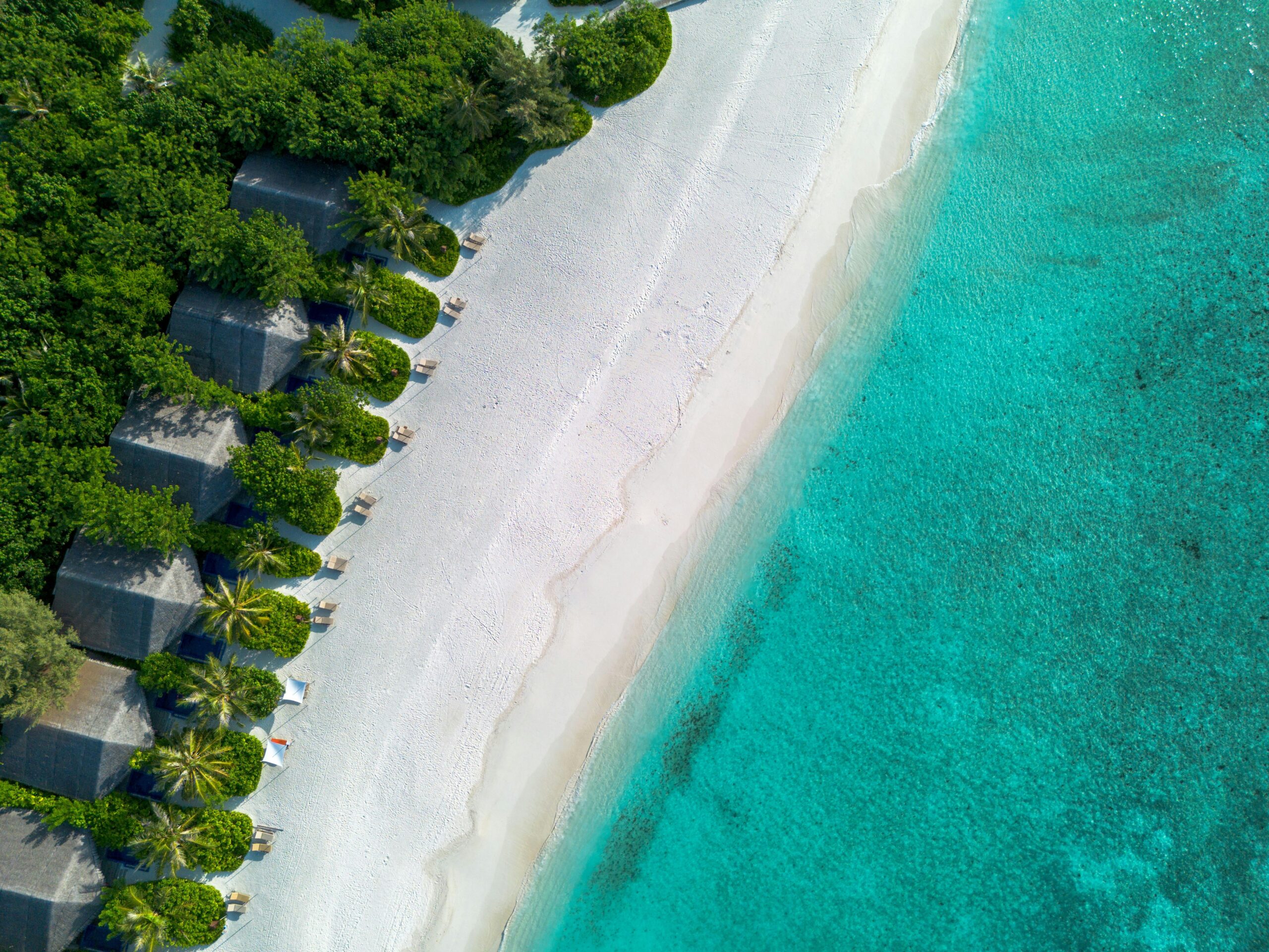 Aerial drone shot of a tropical resort with vibrant blue waters and white sandy beach.