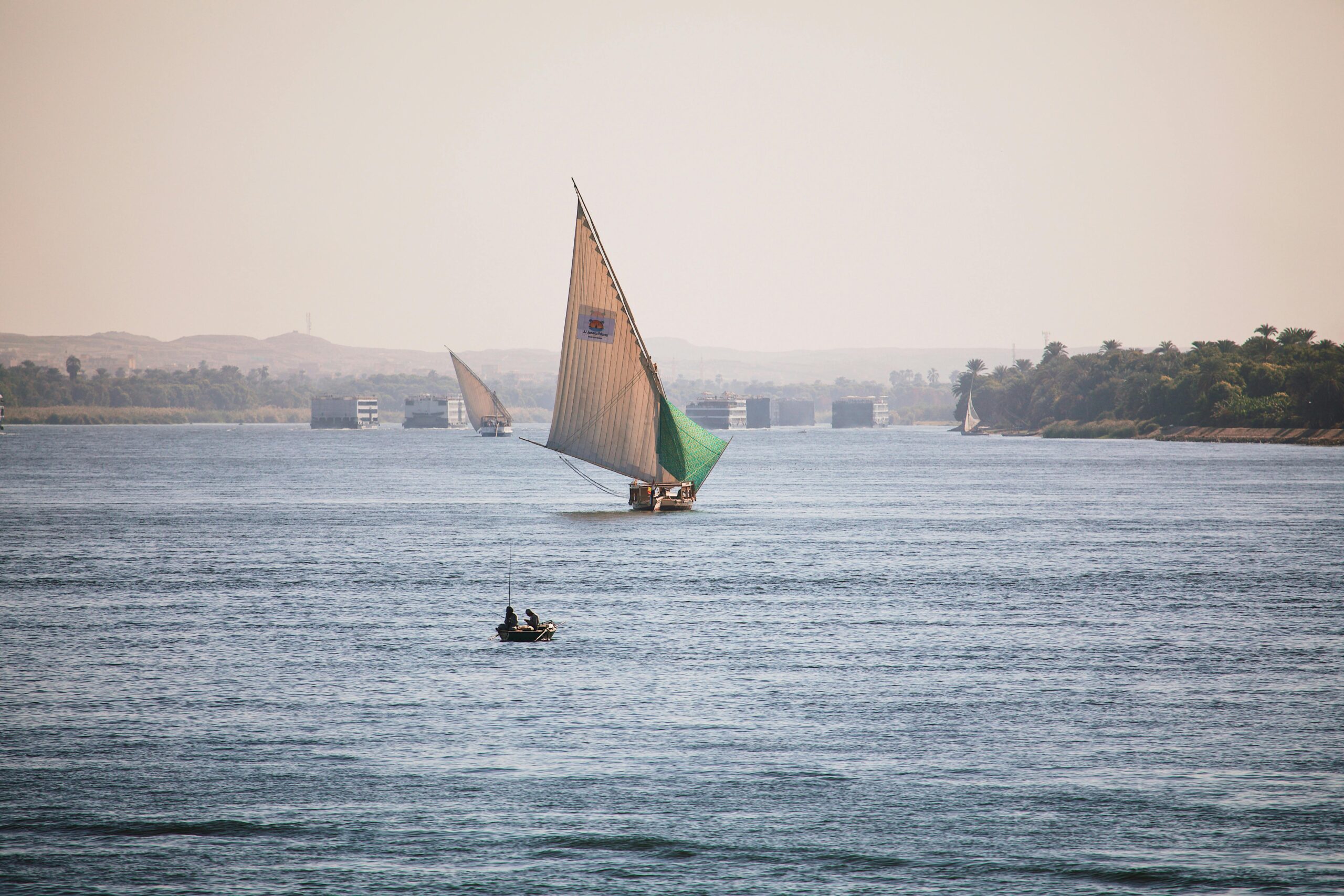 A scenic view of a traditional felucca sailing on the Nile River in Luxor, Egypt, under a clear blue sky.