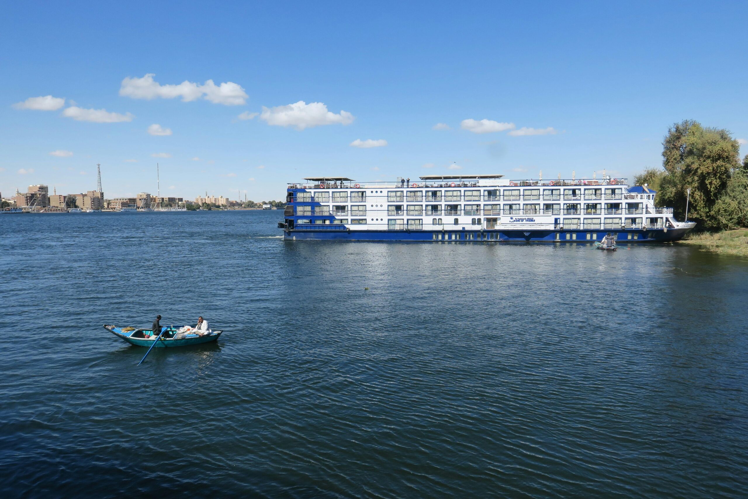 A ferry boat and rowboat on the Nile River under a clear blue sky in Luxor, Egypt.