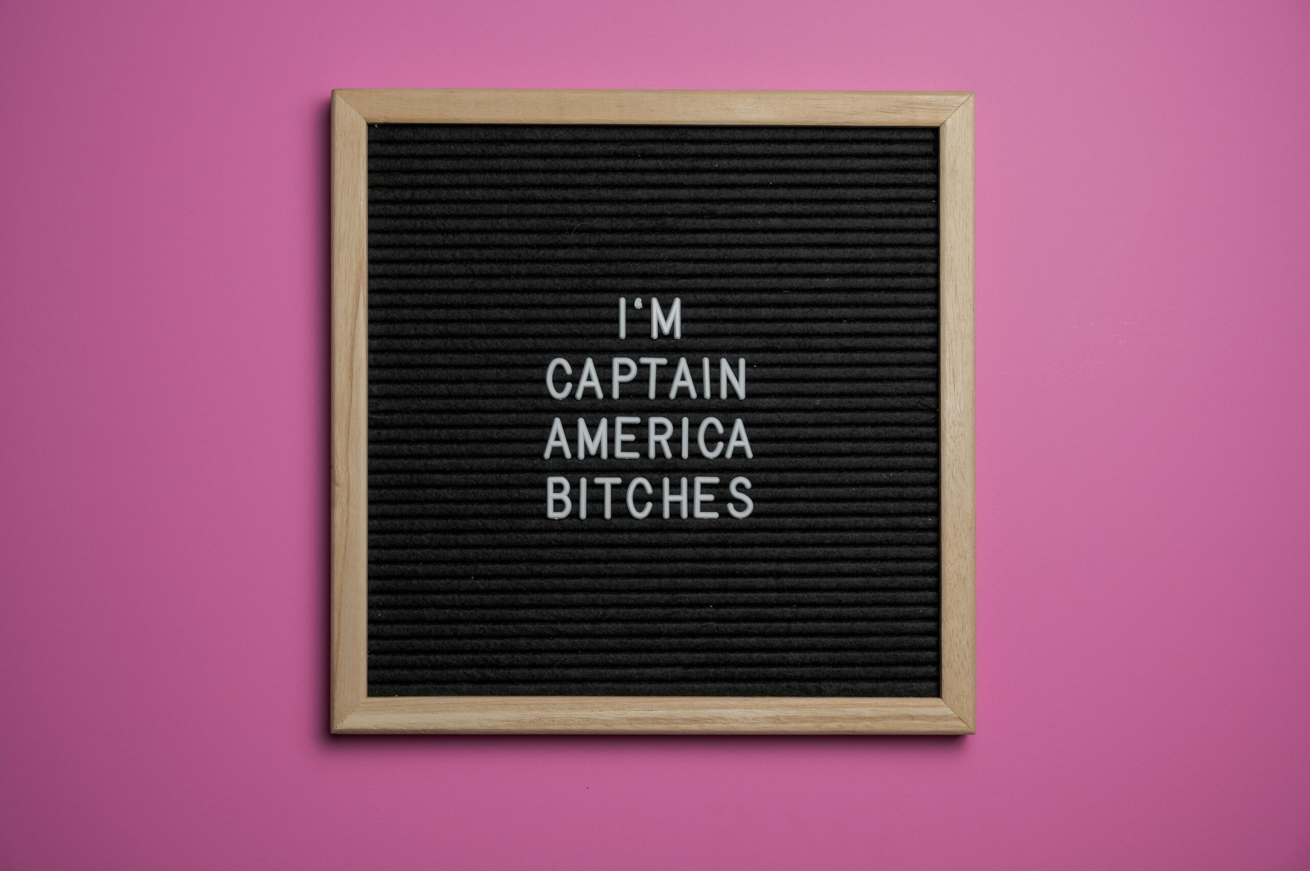 Black and wooden letter board with humorous text against a pink wall.