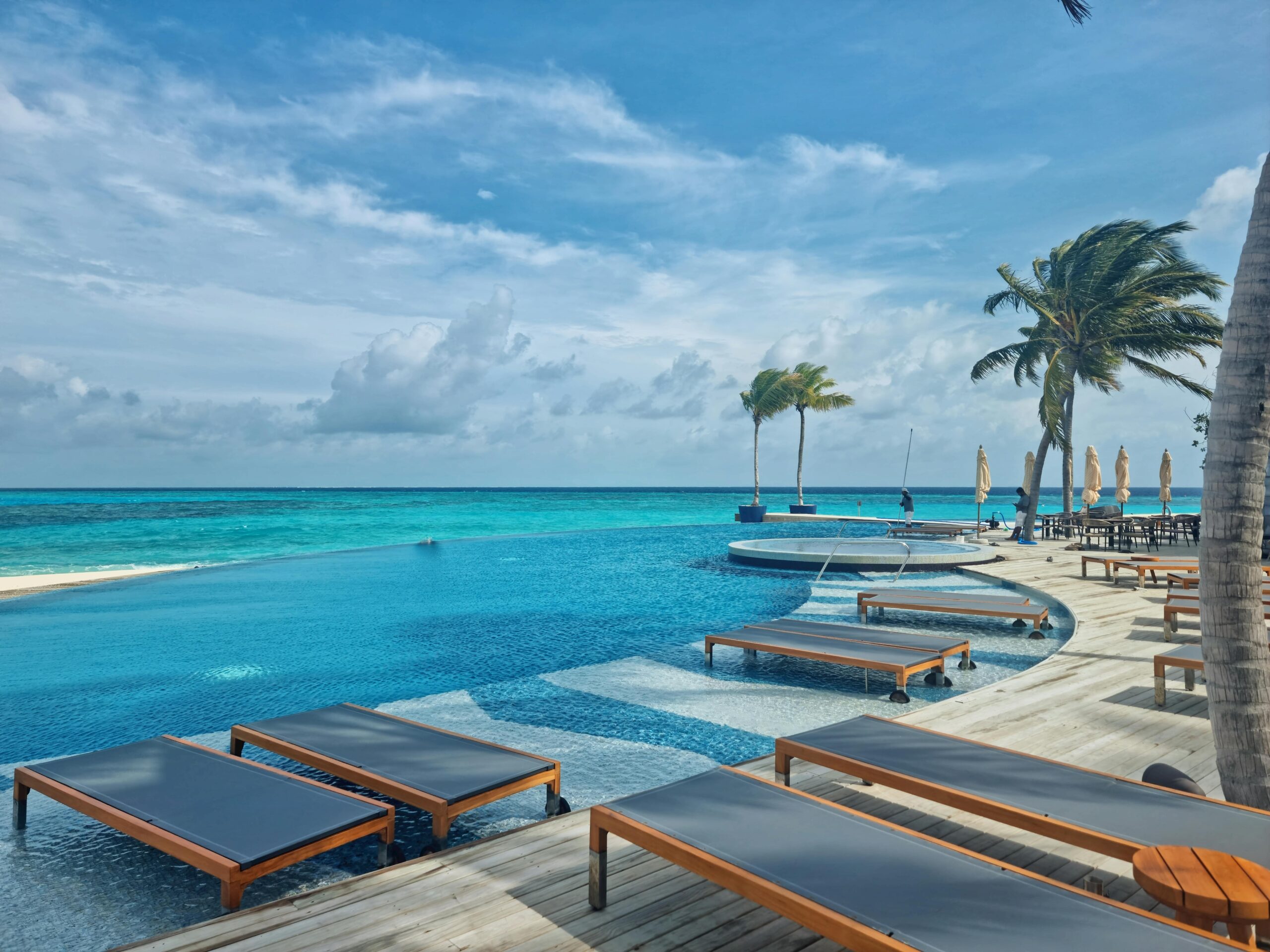 Relax by the stunning infinity pool at a luxury resort in the Maldives, surrounded by turquoise waters and palm trees.