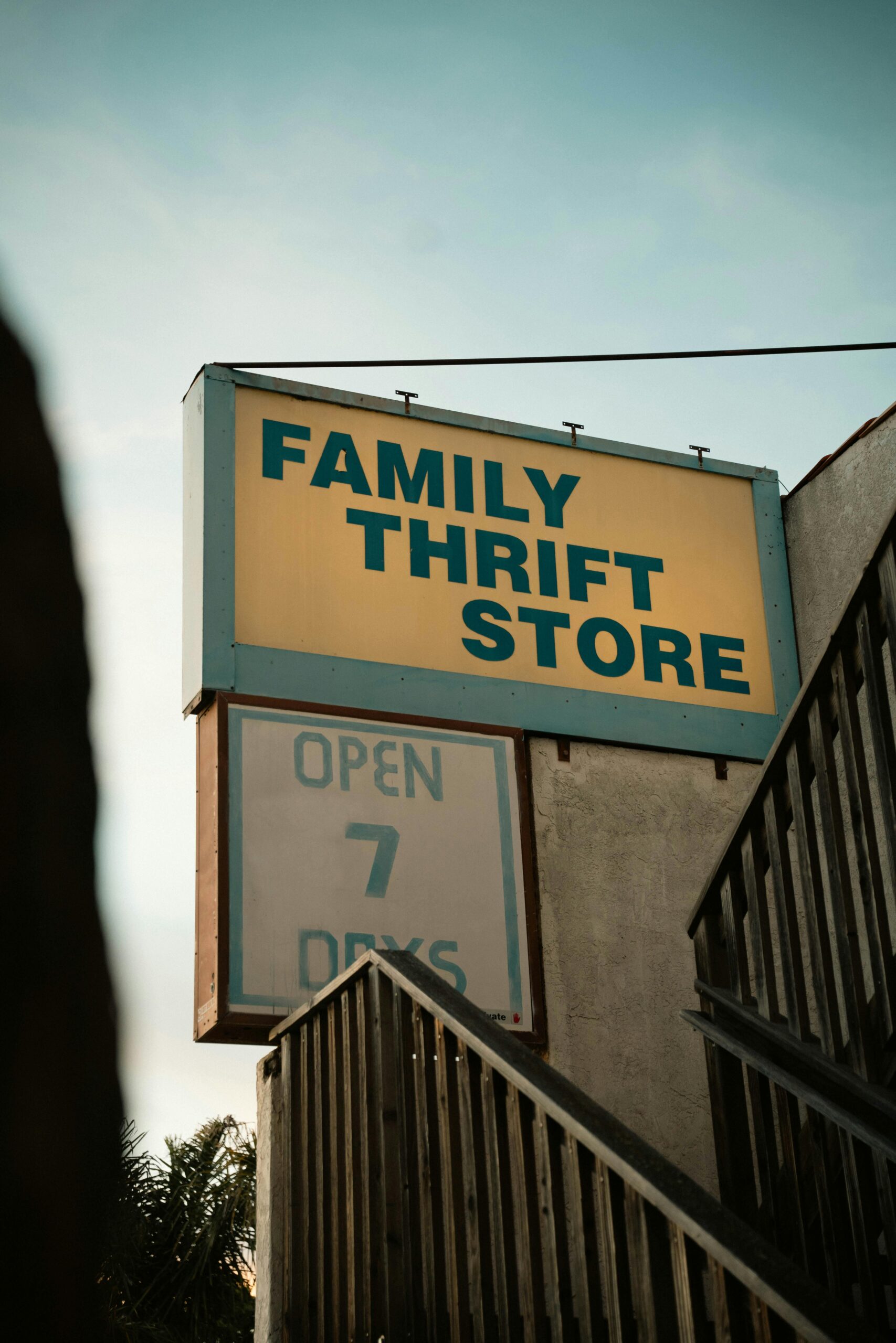 Retro-style sign for a family thrift store with stairs and wooden railing in view.