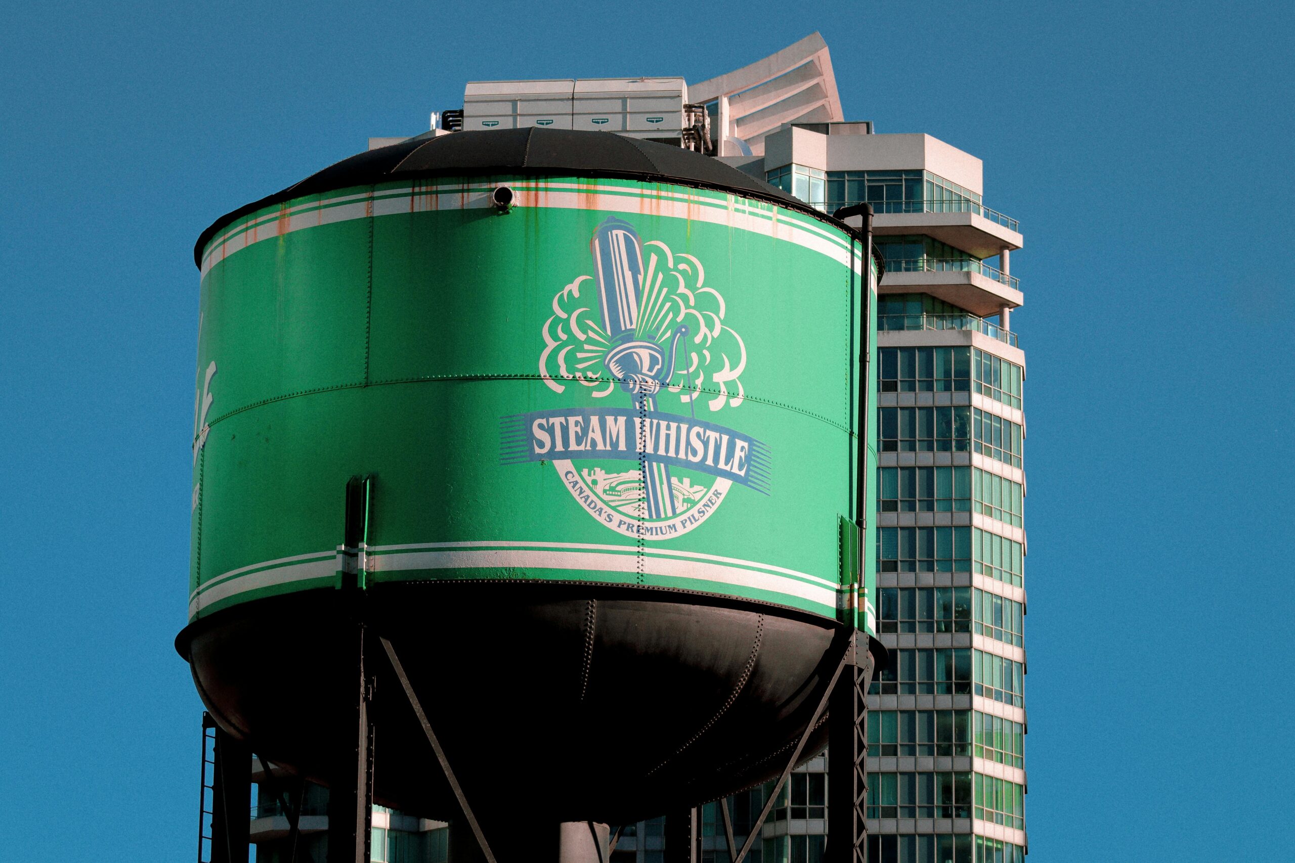 A vibrant green Steam Whistle water tank set against modern Toronto architecture.