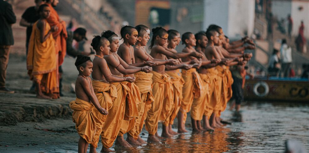 A group of young monks in orange robes perform a ritual by the Ganges River in Varanasi, India.