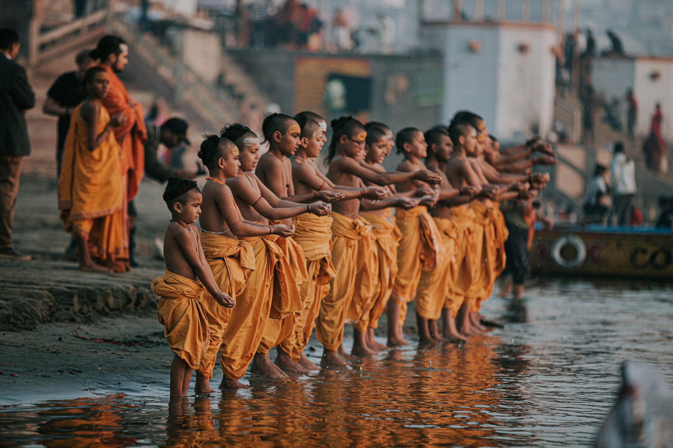 A group of young monks in orange robes perform a ritual by the Ganges River in Varanasi, India.