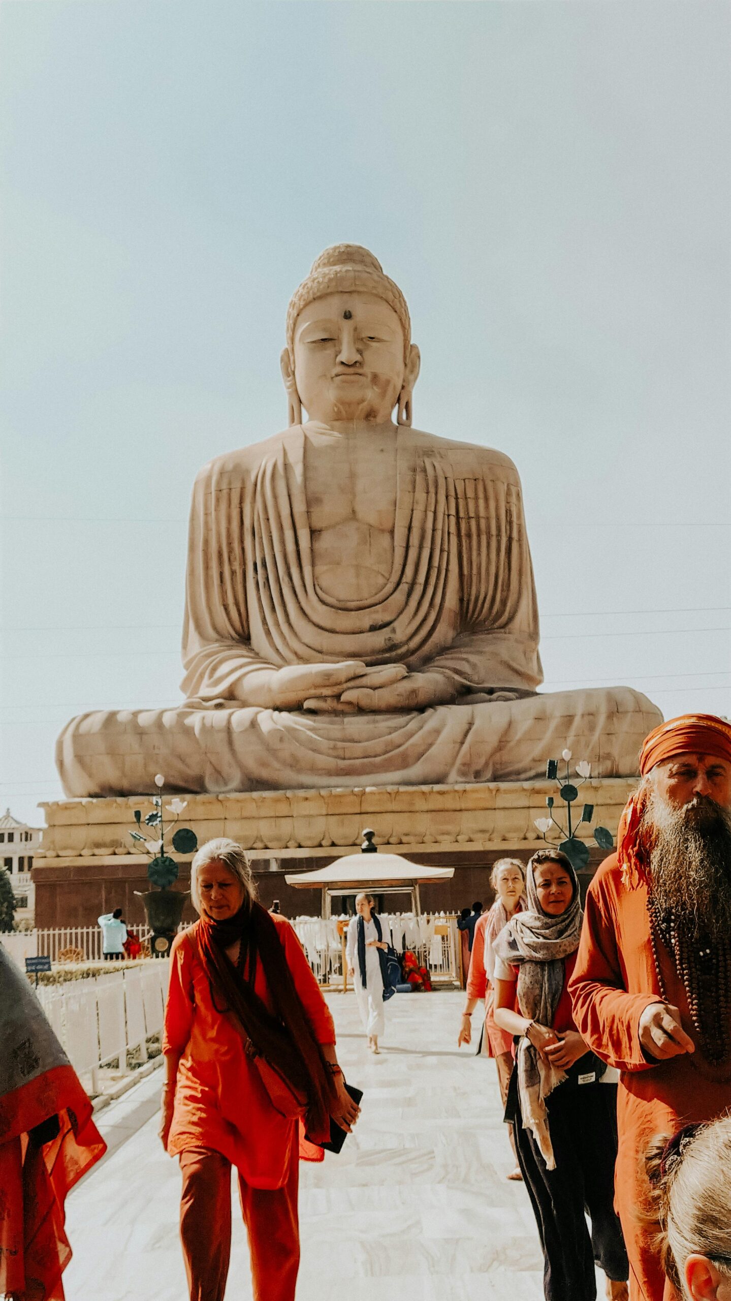 Group of pilgrims at the Giant Buddha statue in Bodh Gaya, India, under sunny sky.