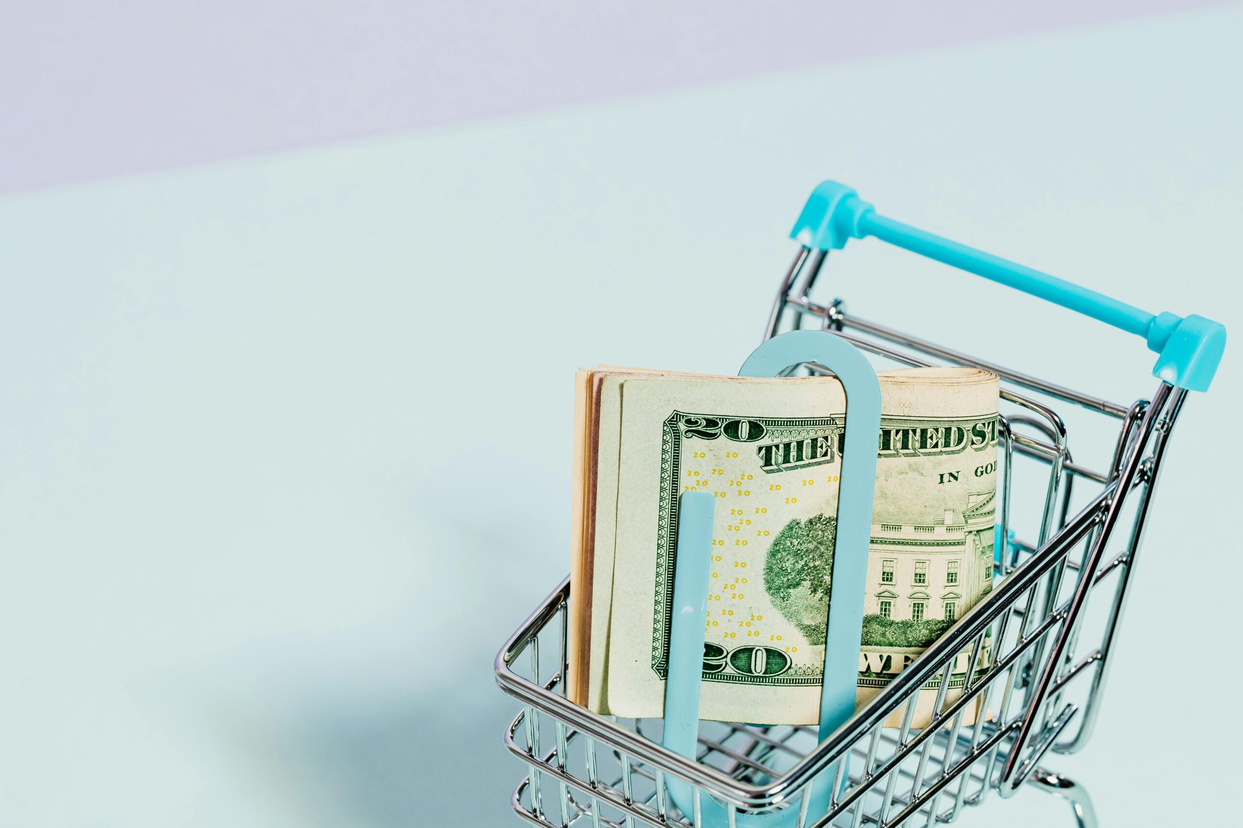 A shopping cart holding a stack of US dollar bills symbolizes financial savings and consumer spending.