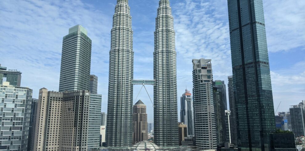 Panoramic view of the iconic Petronas Towers in Kuala Lumpur against a blue sky.