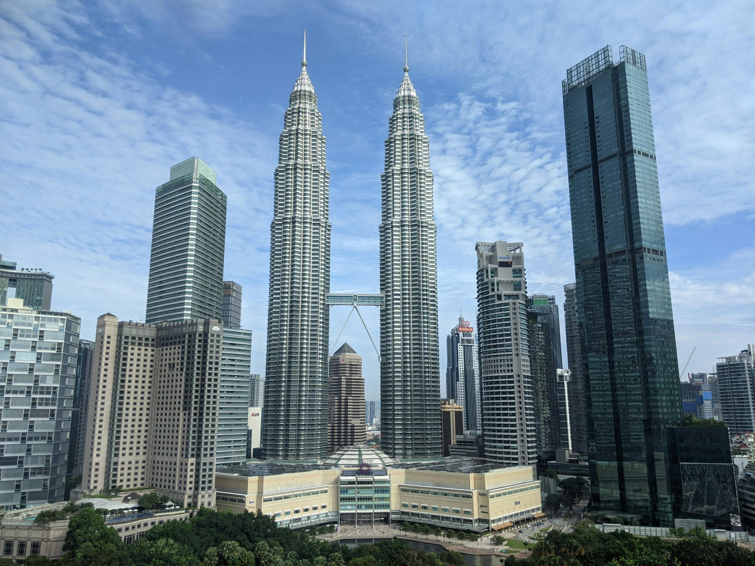 Panoramic view of the iconic Petronas Towers in Kuala Lumpur against a blue sky.