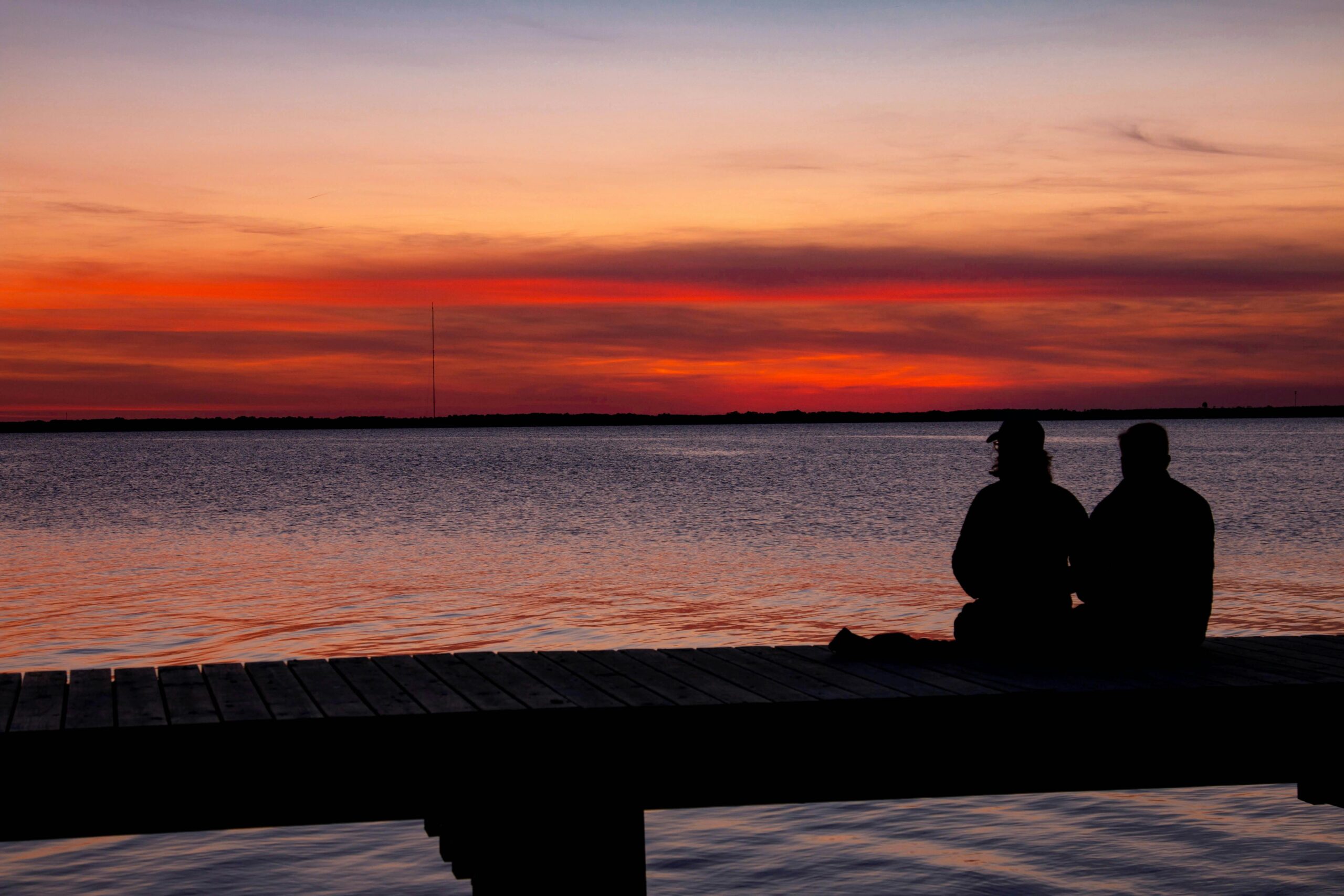 Romantic couple sitting in silhouette enjoying scenic sunset by the sea.