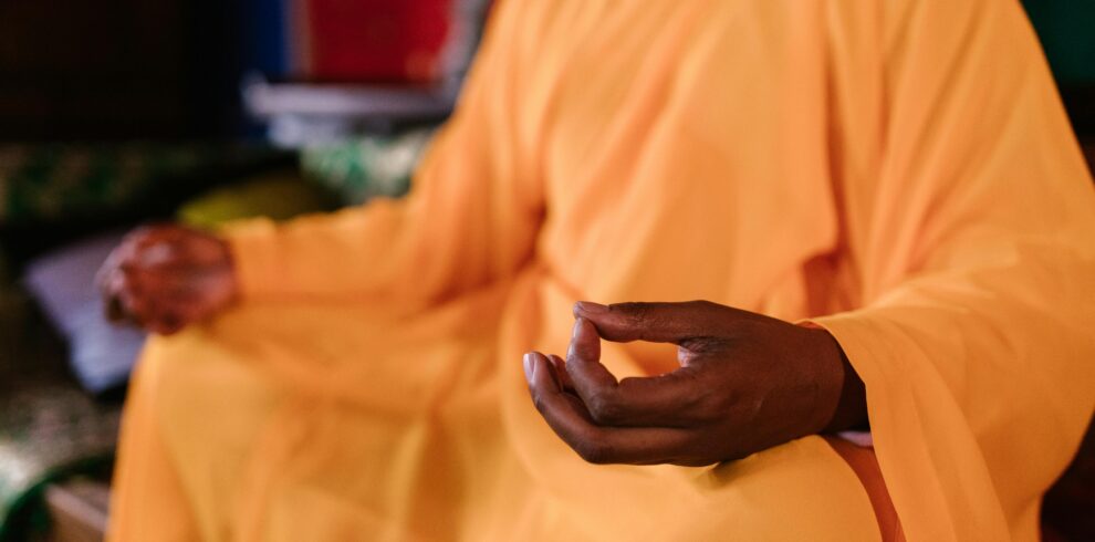 Close-up of a meditating monk in traditional orange robe practicing Zen meditation indoors.