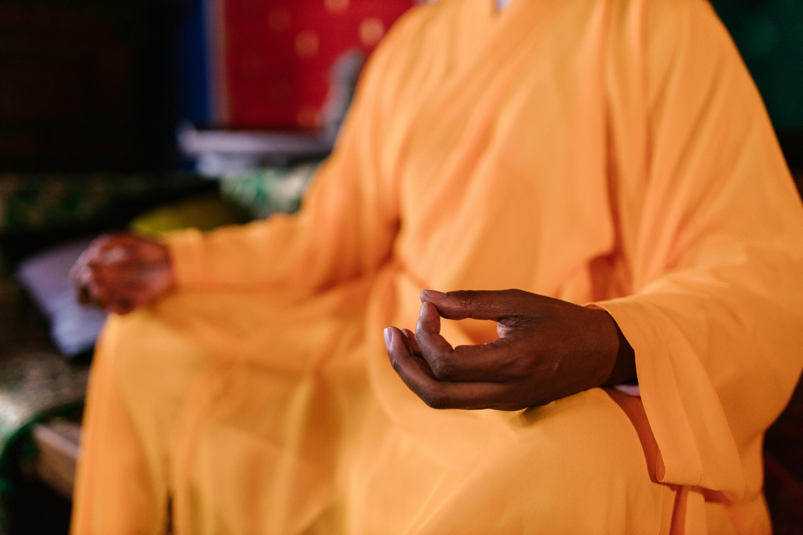 Close-up of a meditating monk in traditional orange robe practicing Zen meditation indoors.