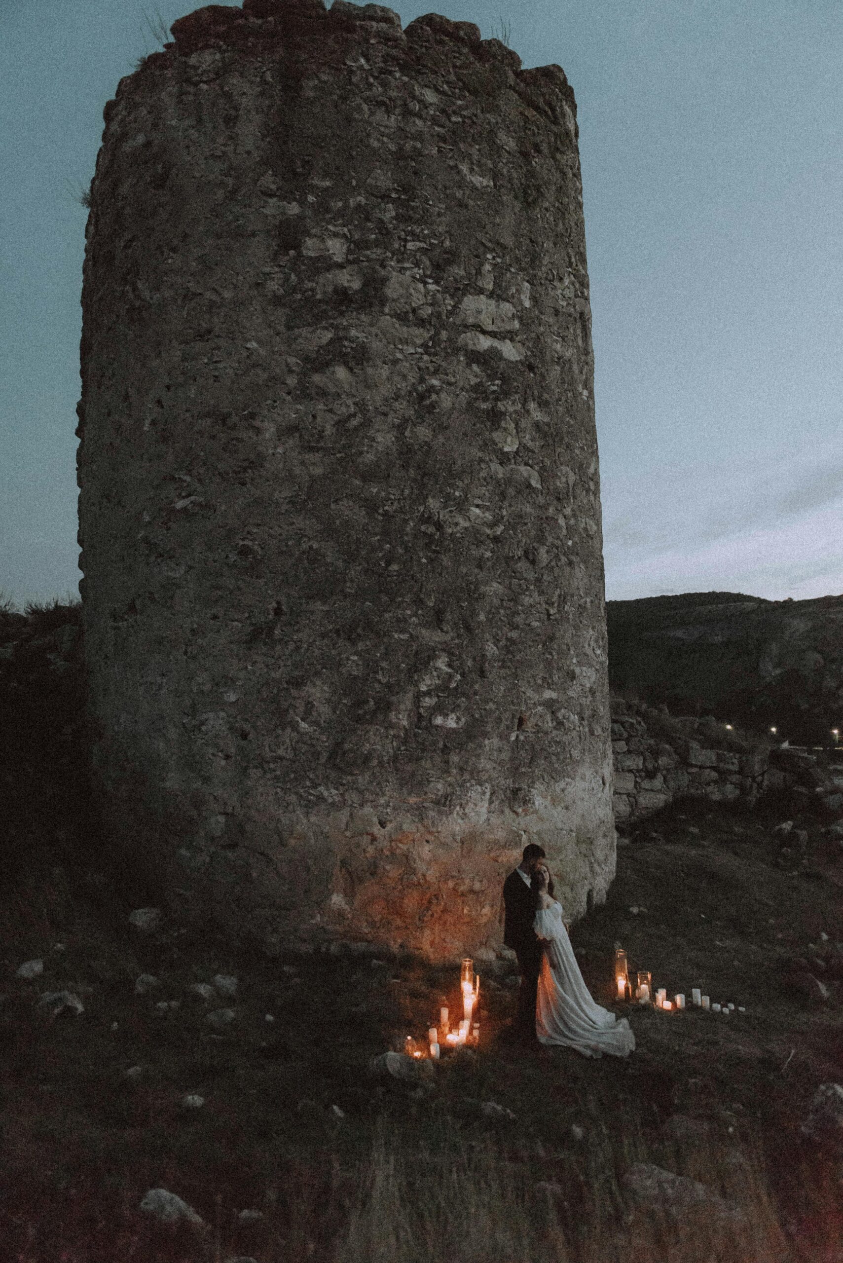Couple embraces by candlelight near ancient tower, capturing timeless romance.