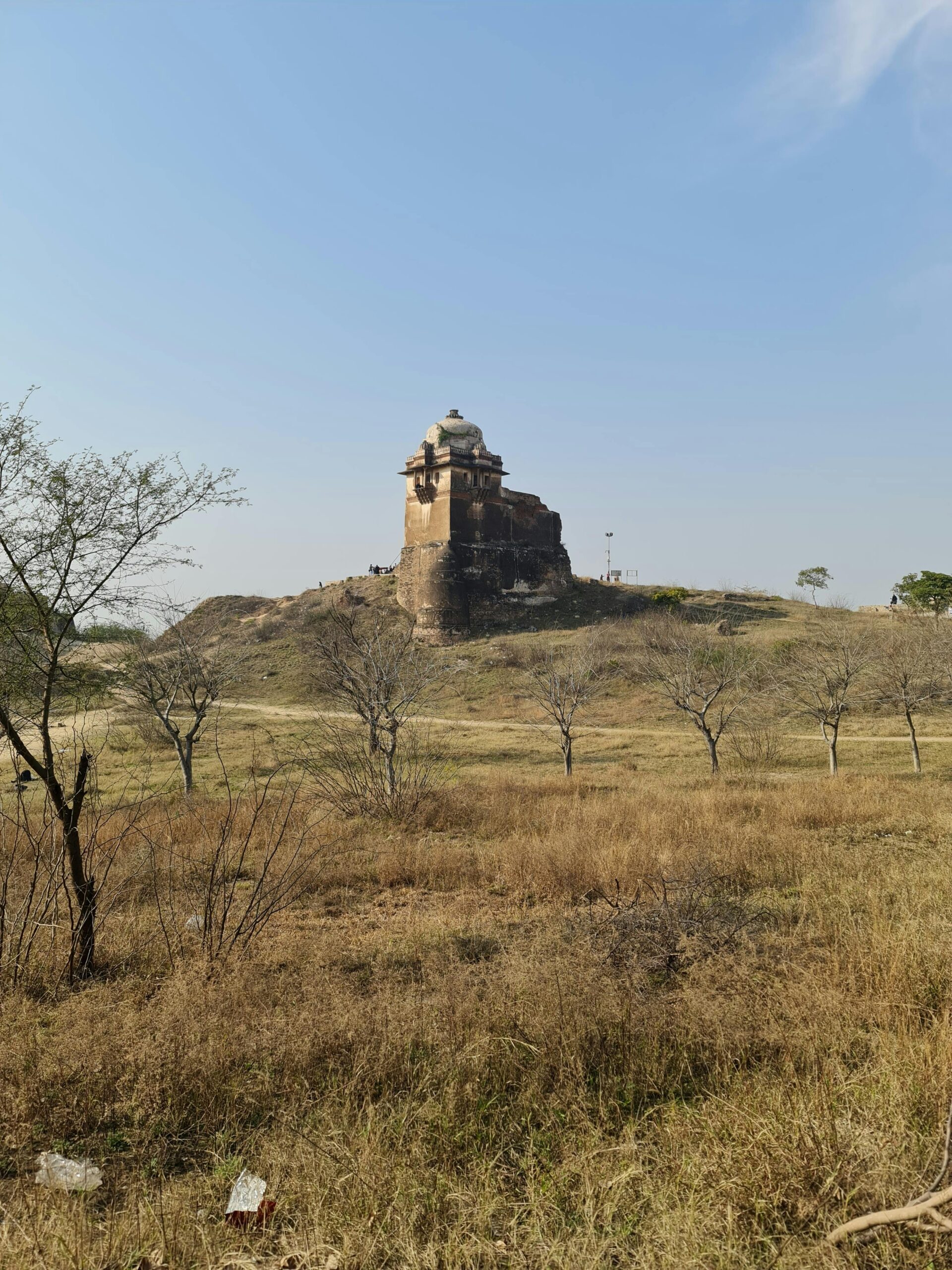 Ancient stone tower in a serene countryside setting under a clear blue sky.
