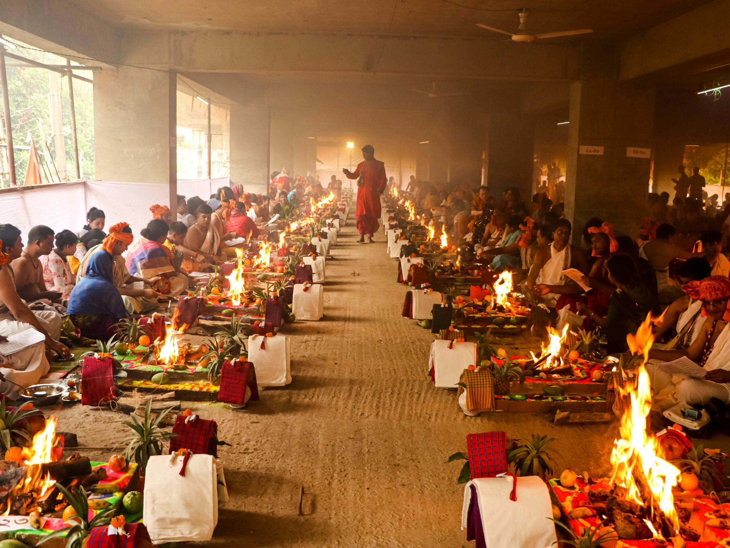 A vibrant and colorful Hindu ritual with participants in traditional attire and ceremonial fires in Dhaka.