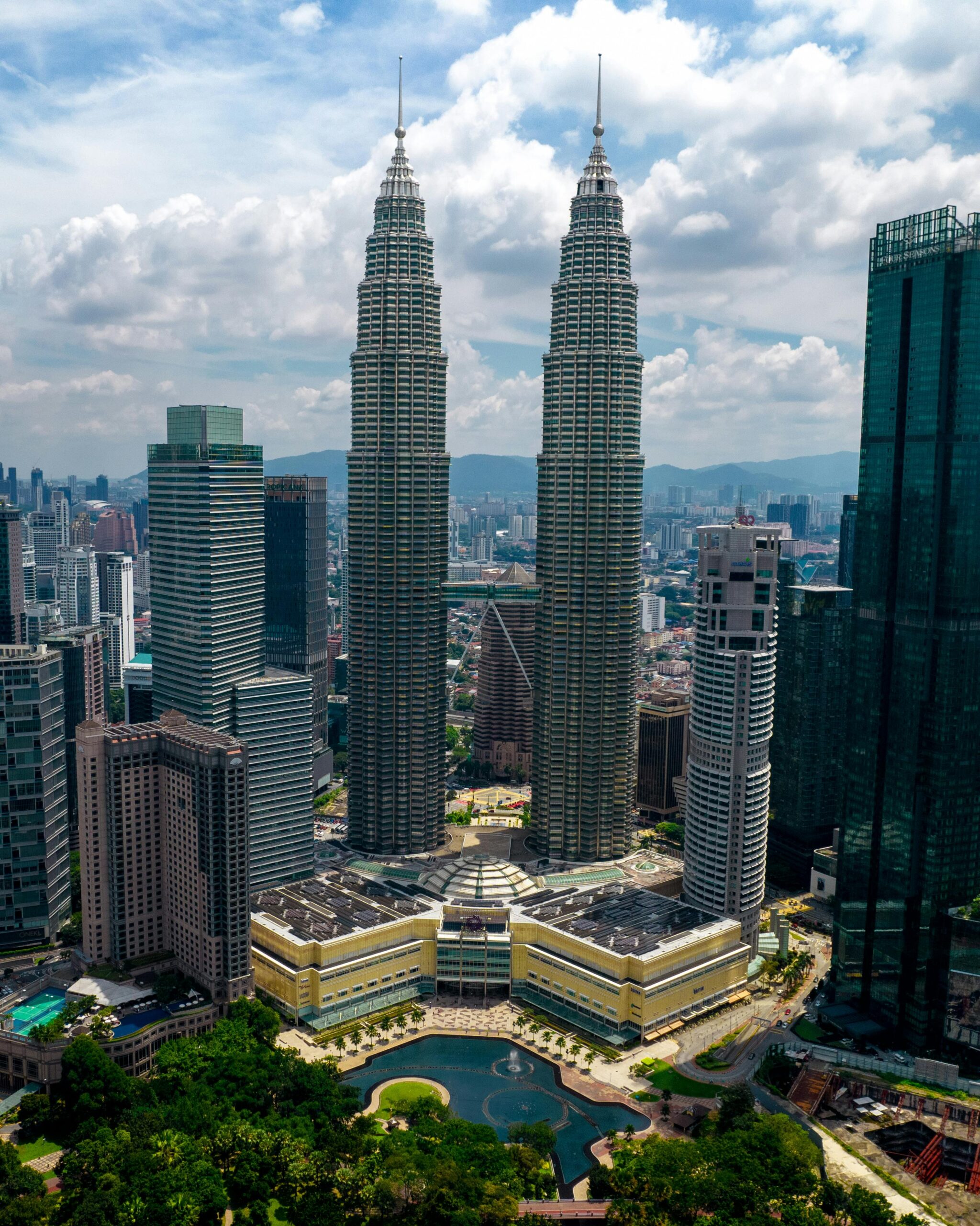 Skyline of Kuala Lumpur featuring the iconic Petronas Twin Towers under a cloudy sky.