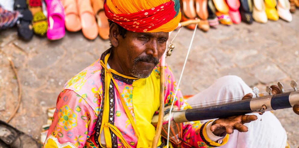 Traditional Rajasthani musician playing an instrument outdoors at a cultural event.