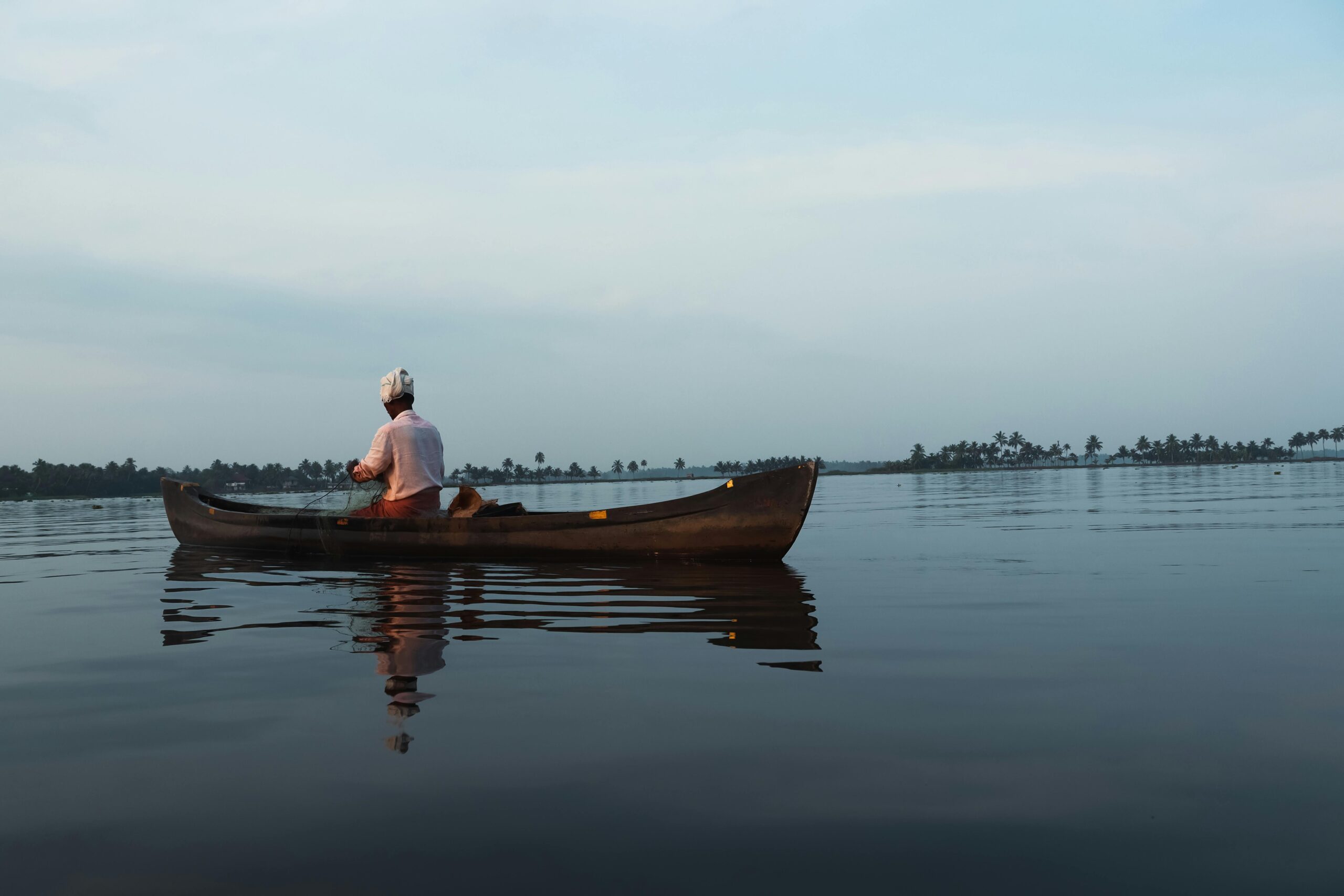 A man paddling a canoe on the serene Alappuzha backwaters at dawn, India.