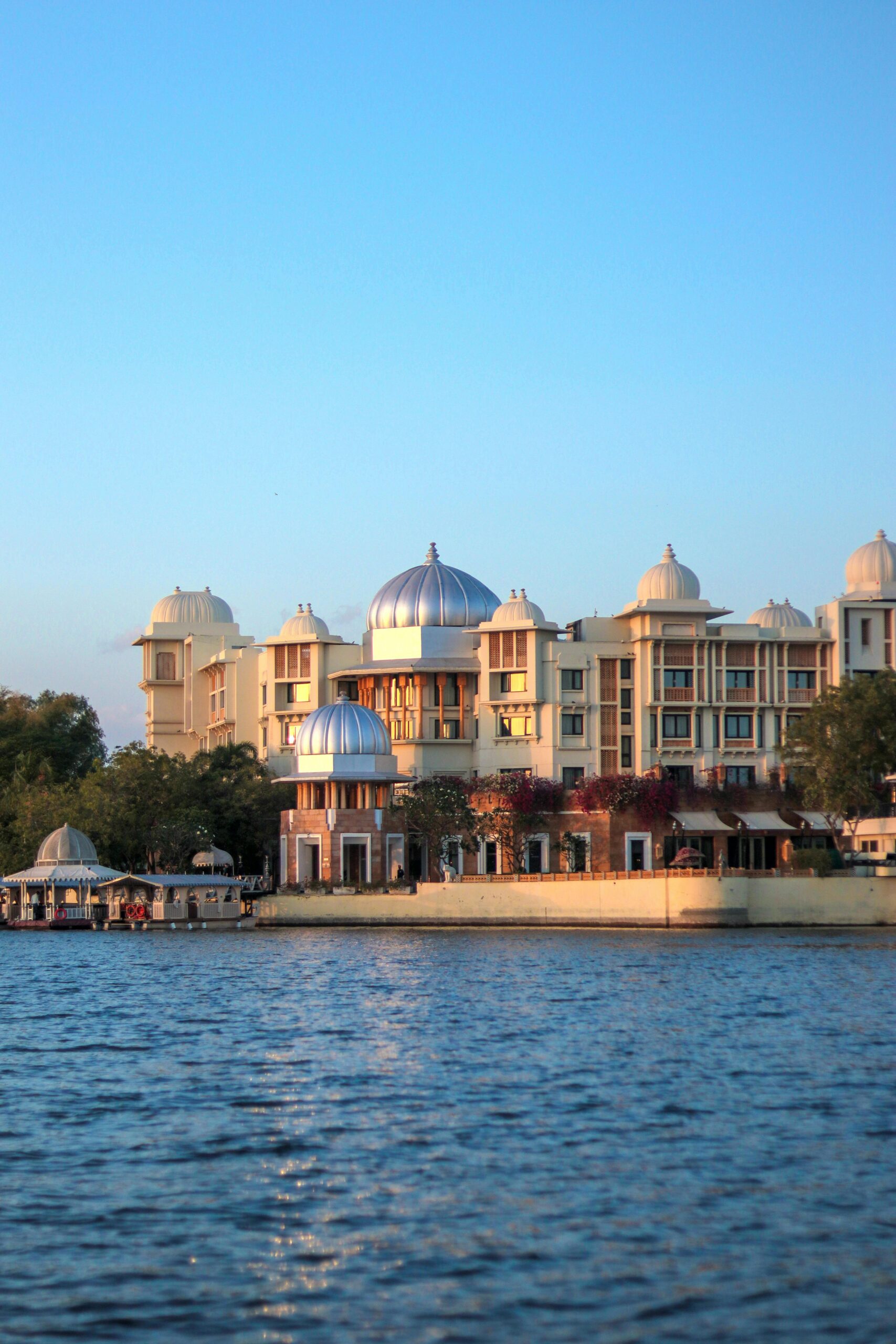 Scenic view of the Leela Palace Udaipur by Lake Pichola during sunset, showcasing its unique architecture.