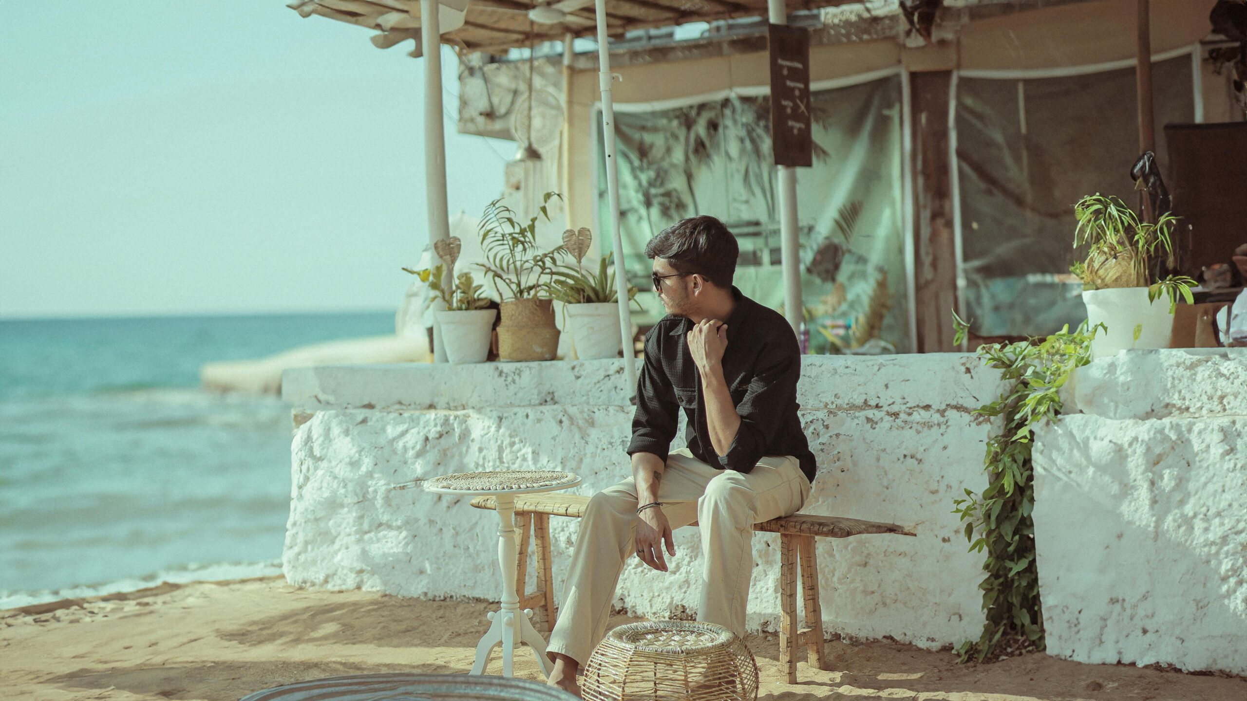 Man sitting at a beachside café in Goa, India, with ocean backdrop and potted plants.