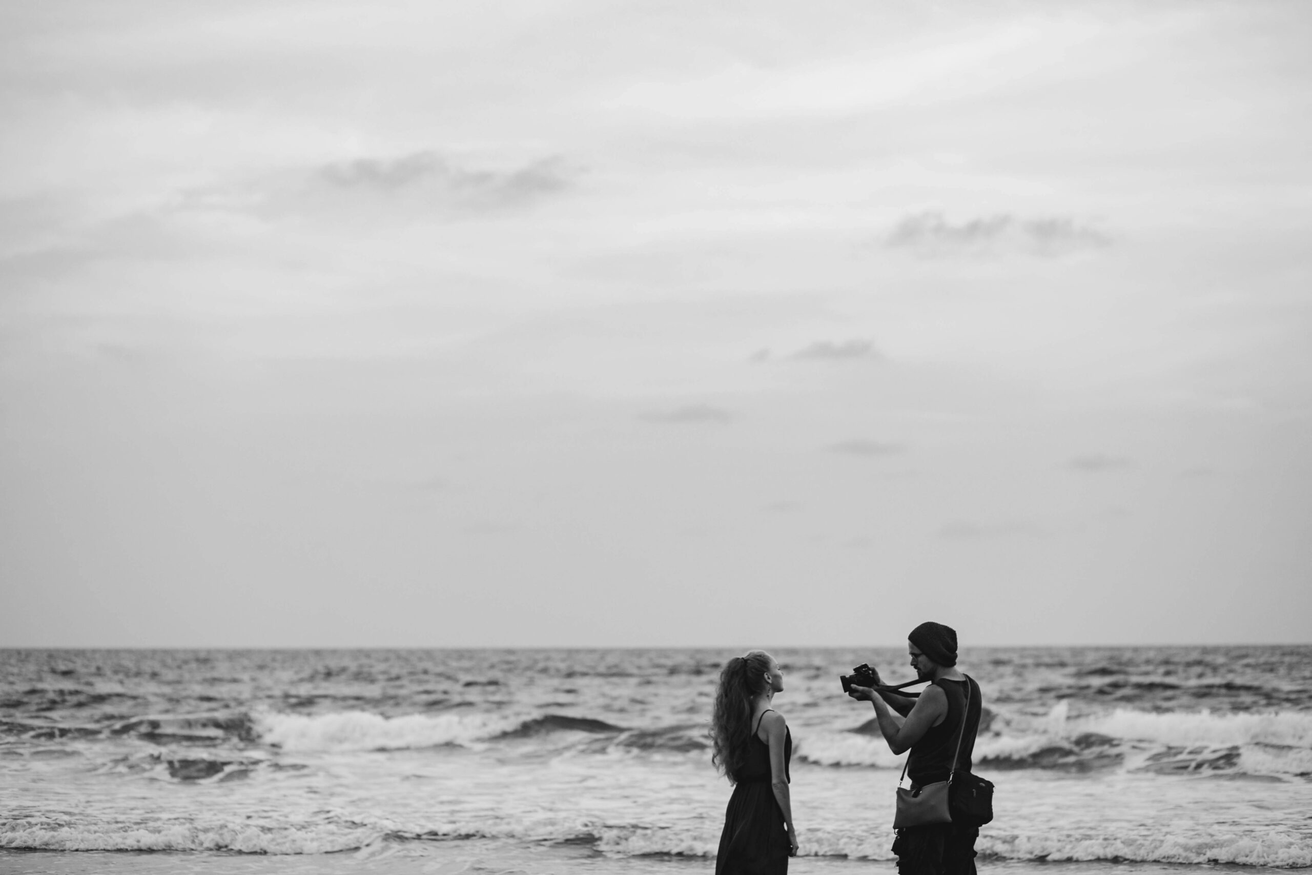 A couple captures memories by the sea in Goa. Black and white photography emphasizing the waves.