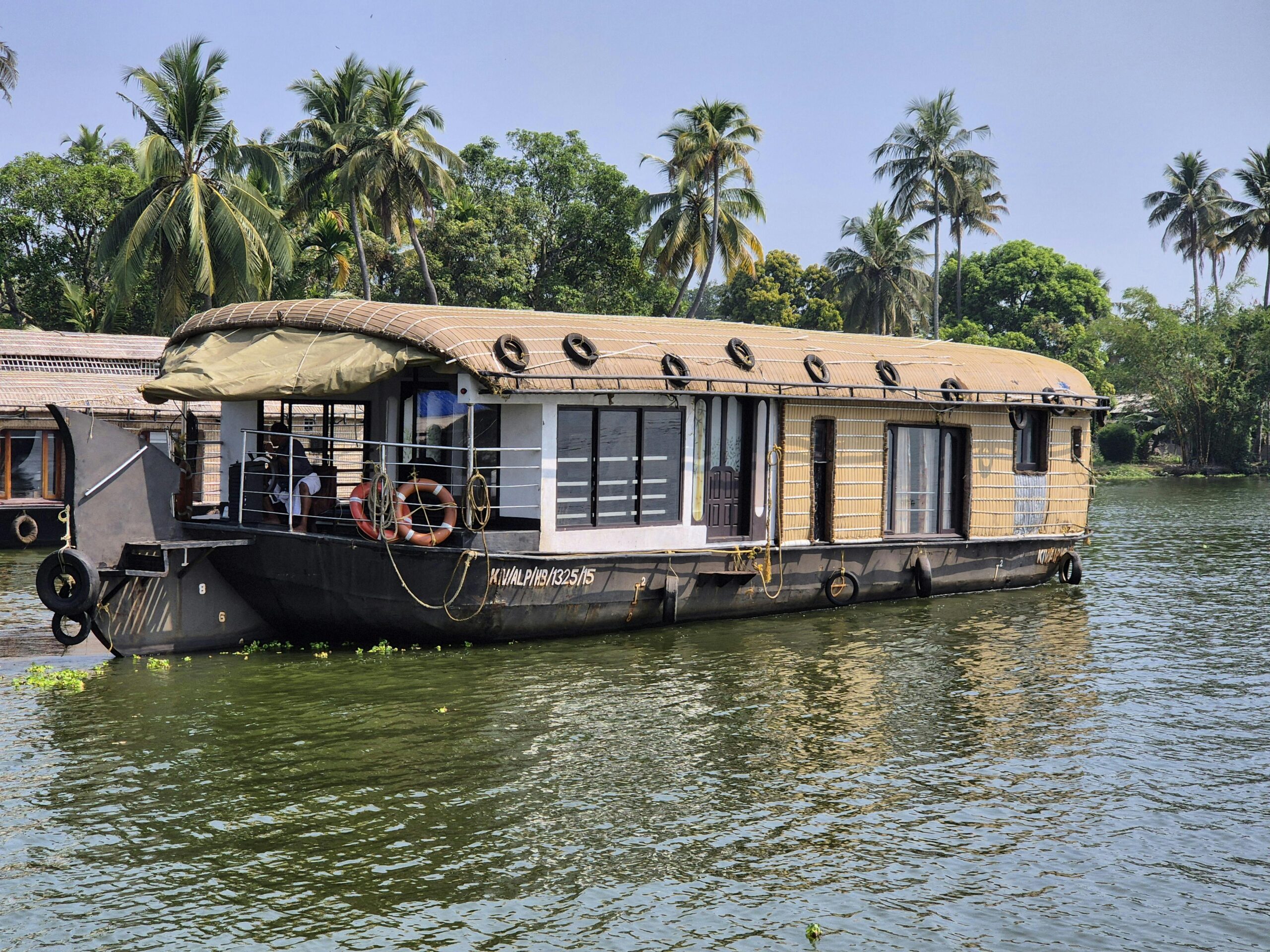 Charming houseboat floating on Kerala backwaters surrounded by tropical palm trees.