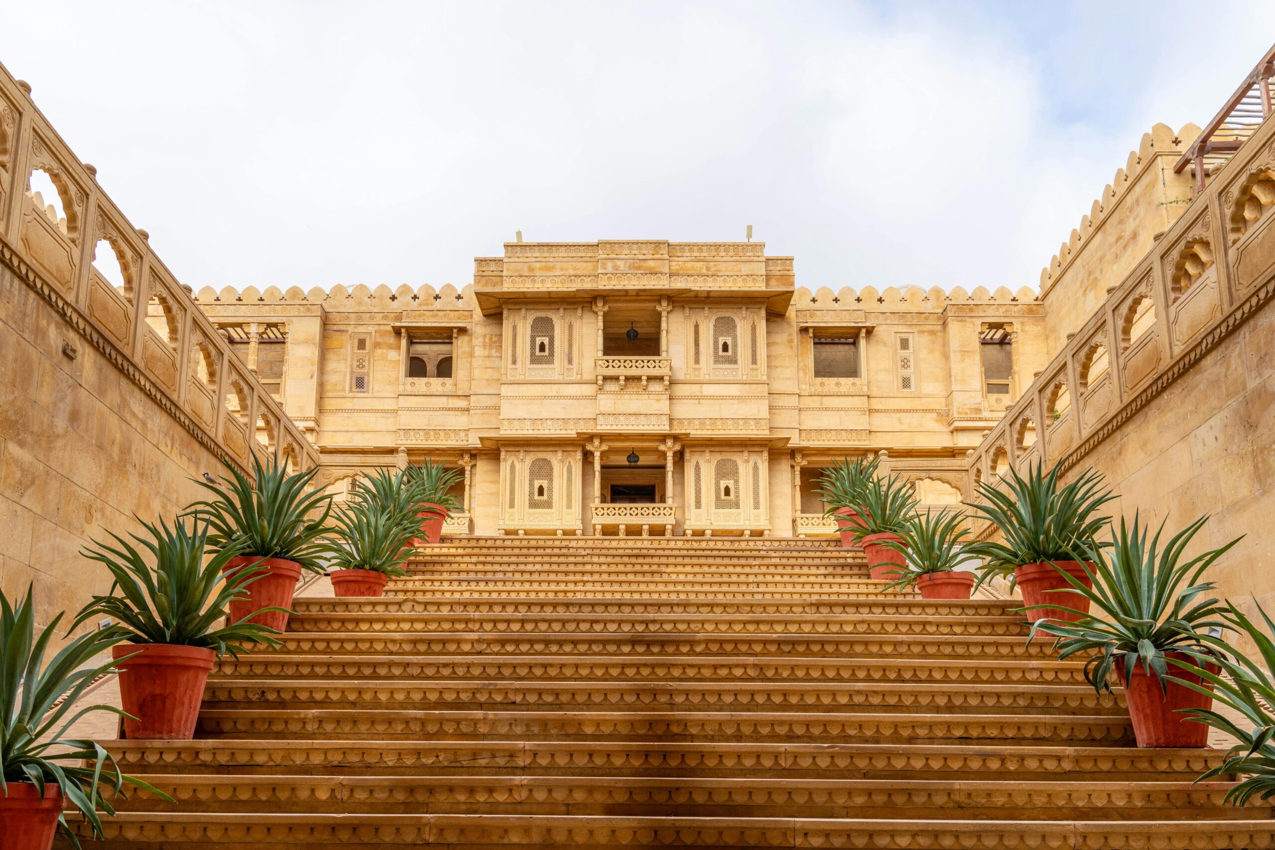 Stunning sandstone palace entrance in Jaisalmer, Rajasthan, India, with ornate steps and potted plants.