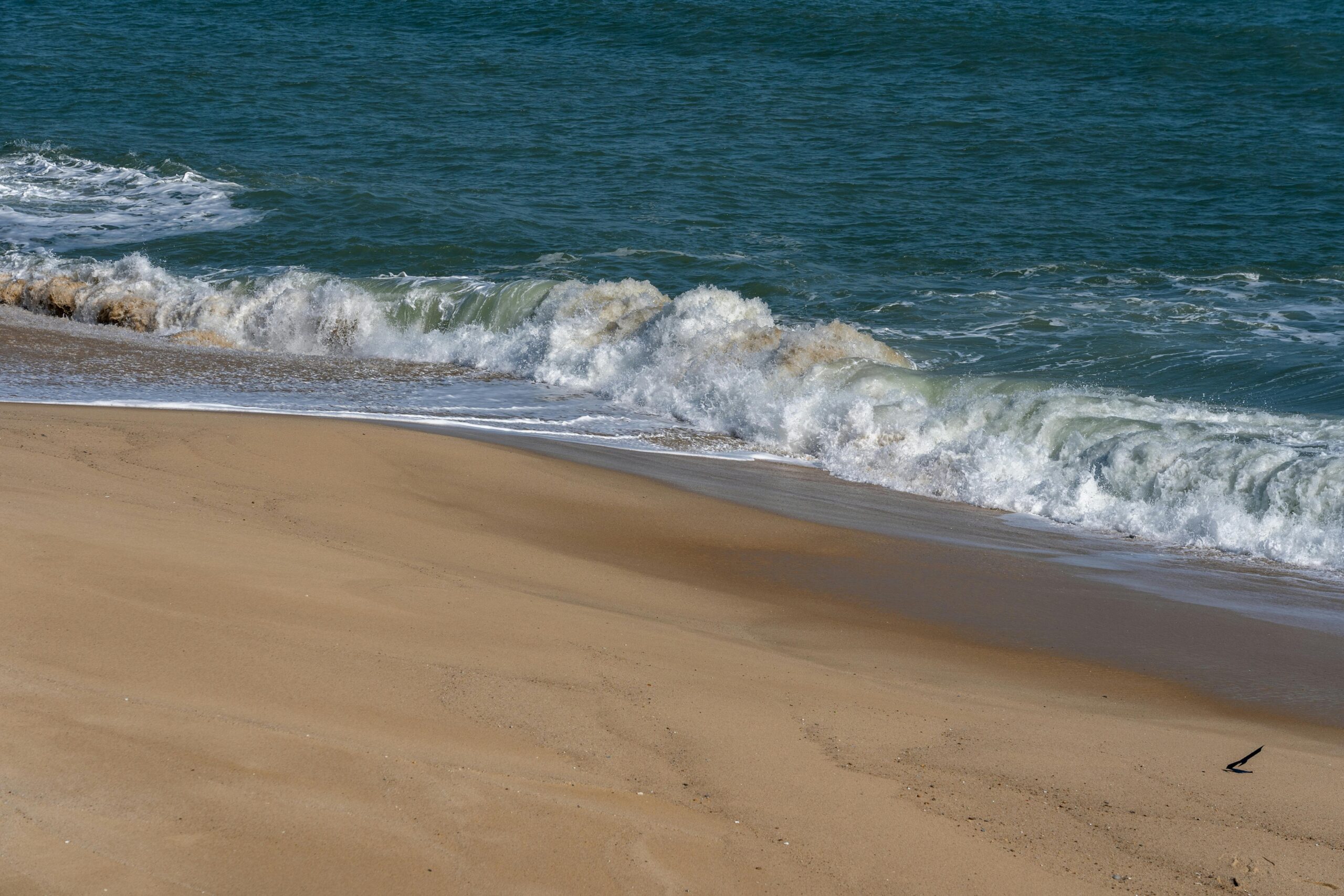 A serene scene of waves gently crashing onto a sandy beach under the daytime sun.