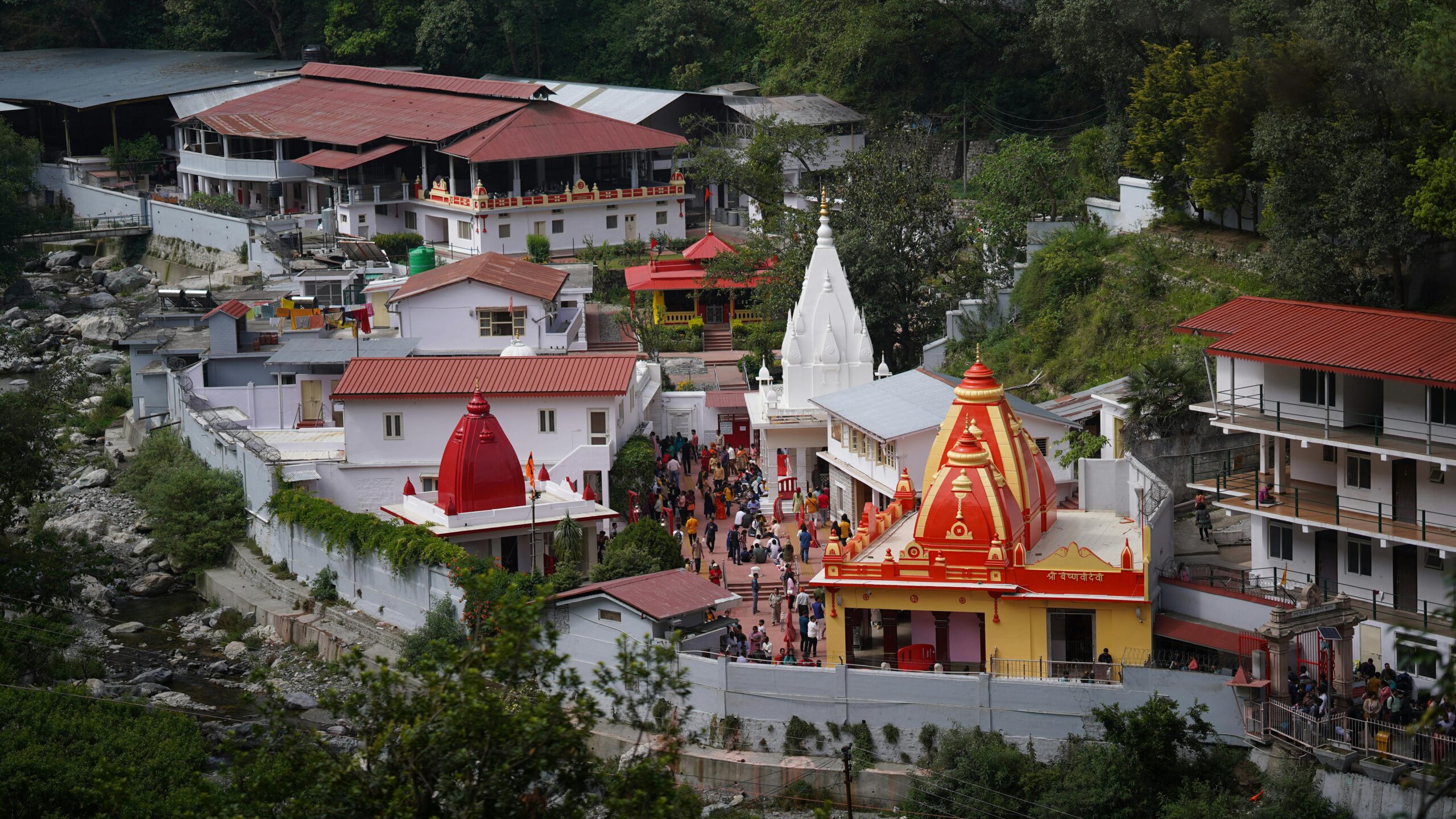 A vibrant aerial shot of the famous Kainchi Dham Temple complex surrounded by lush greenery in Uttarakhand.