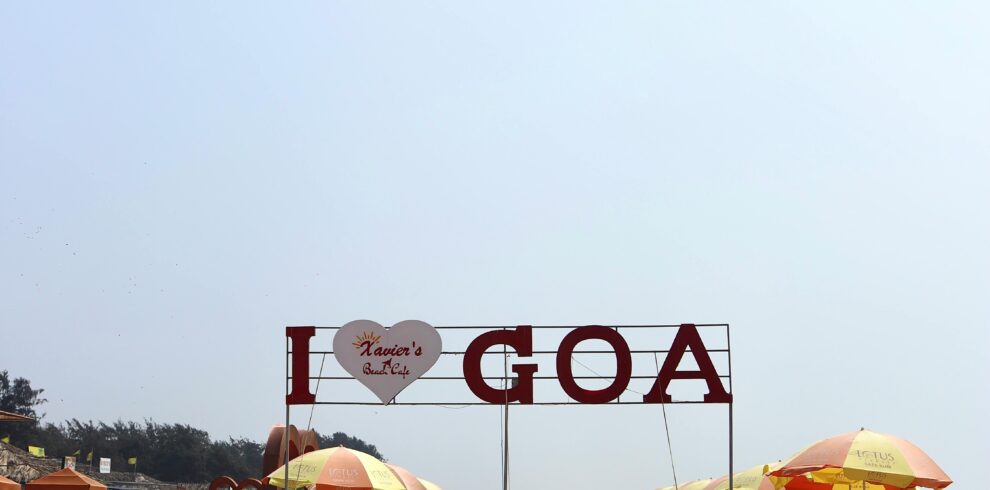 Relaxing beach scene in Goa, India, featuring colorful umbrellas and a sign reading 'I Heart Goa'.