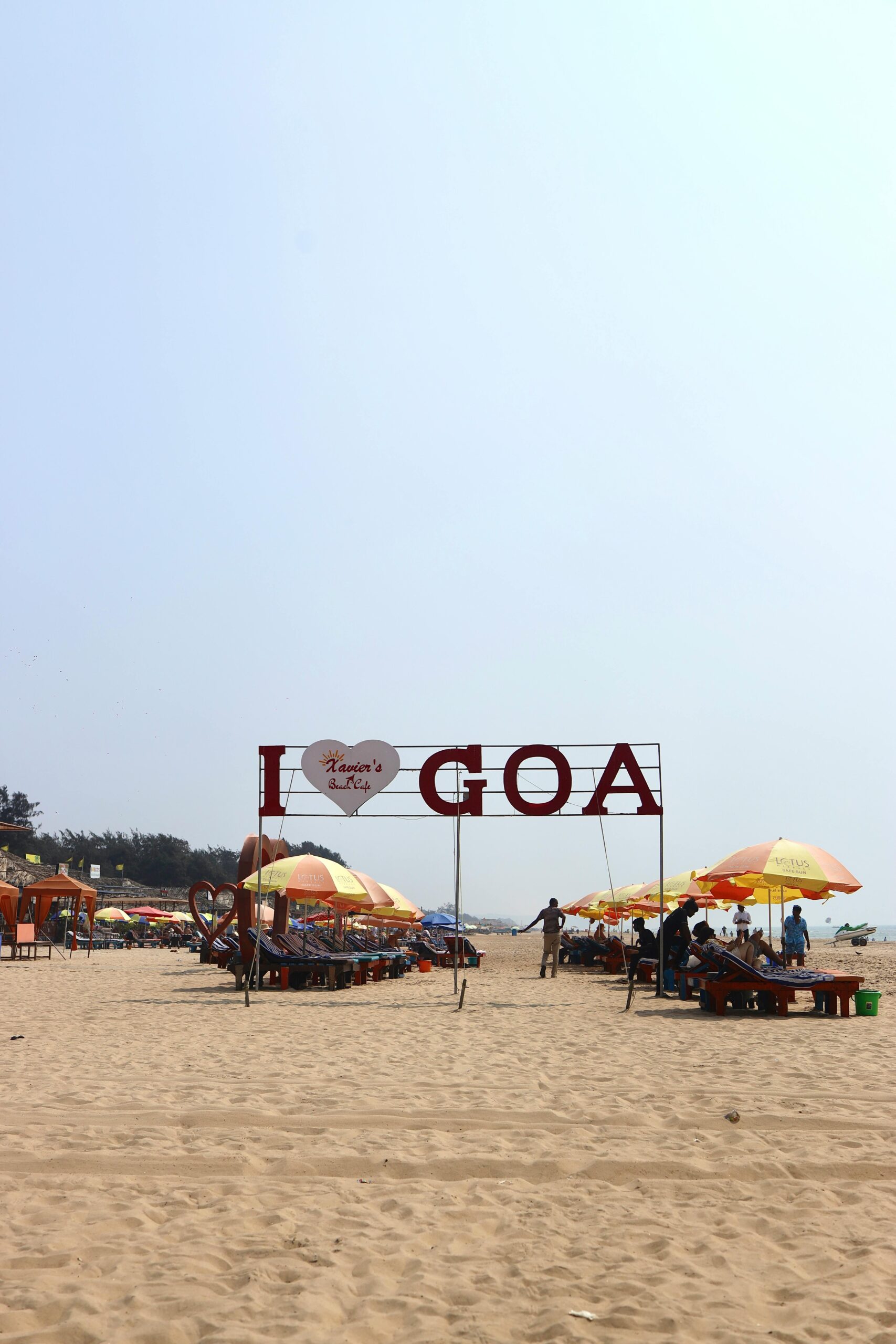 Relaxing beach scene in Goa, India, featuring colorful umbrellas and a sign reading 'I Heart Goa'.